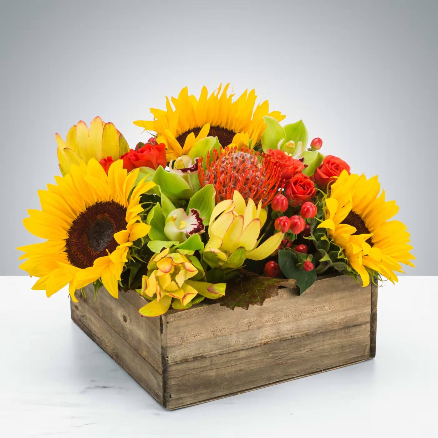 Picnic - Summer in a box! Everybody loves a picnic! Featuring sunflowers, a pincushion protea, and cymbidium orchids, this arrangement is a great option to send to somebody celebrating the summer season.  Approximate Dimensions: 12"D x 8"H