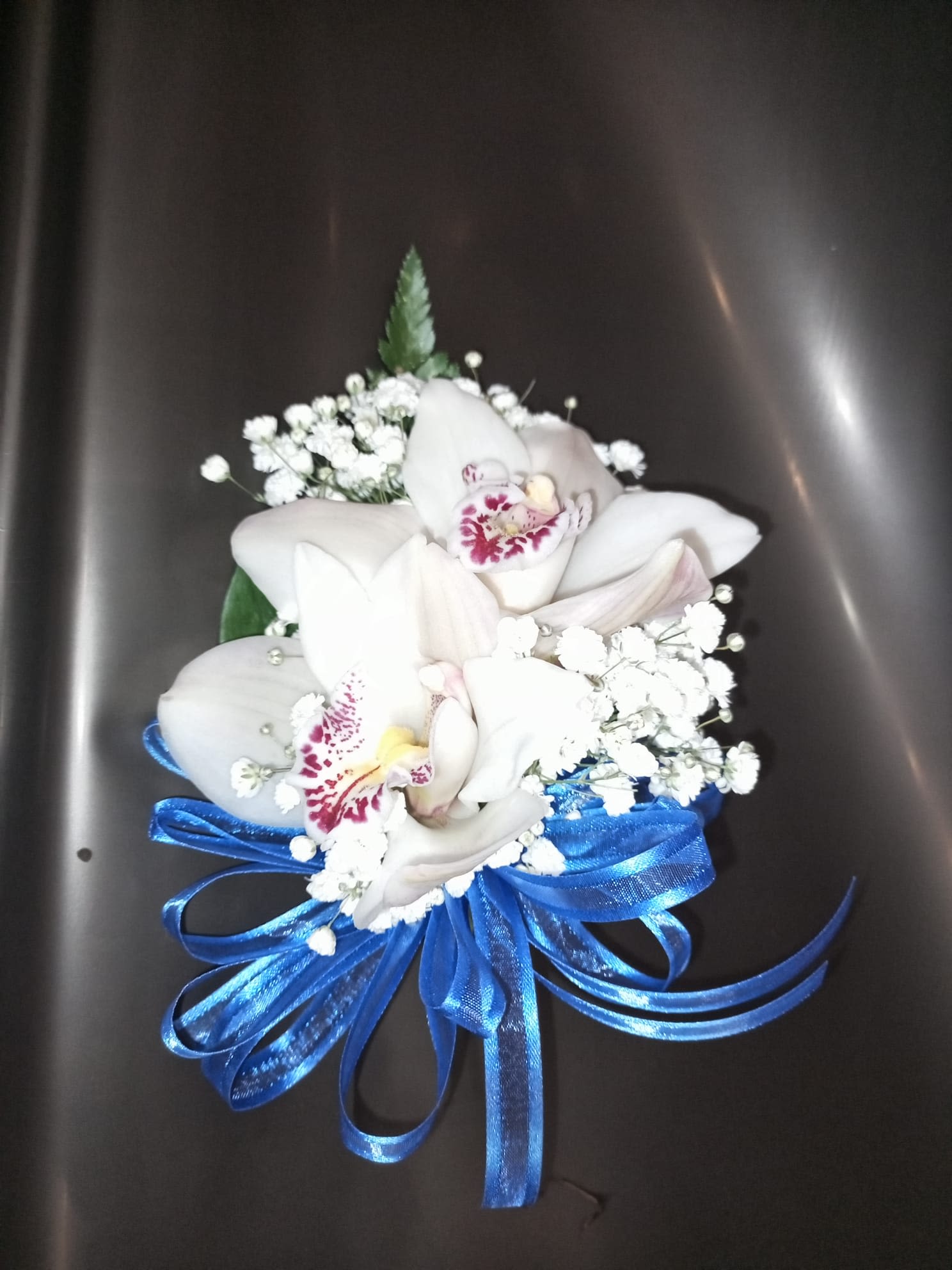 Blue orchid Dream - Tropical elegance with a modern touch. The Blue Orchid Dream corsage combines the exotic beauty of white orchids with gypsophila details and a shiny bow in electric blue, creating a fresh and charming contrast.  Ideal for graduations, weddings, quinceañeras or any special event where you want to stand out with a unique and sophisticated style.