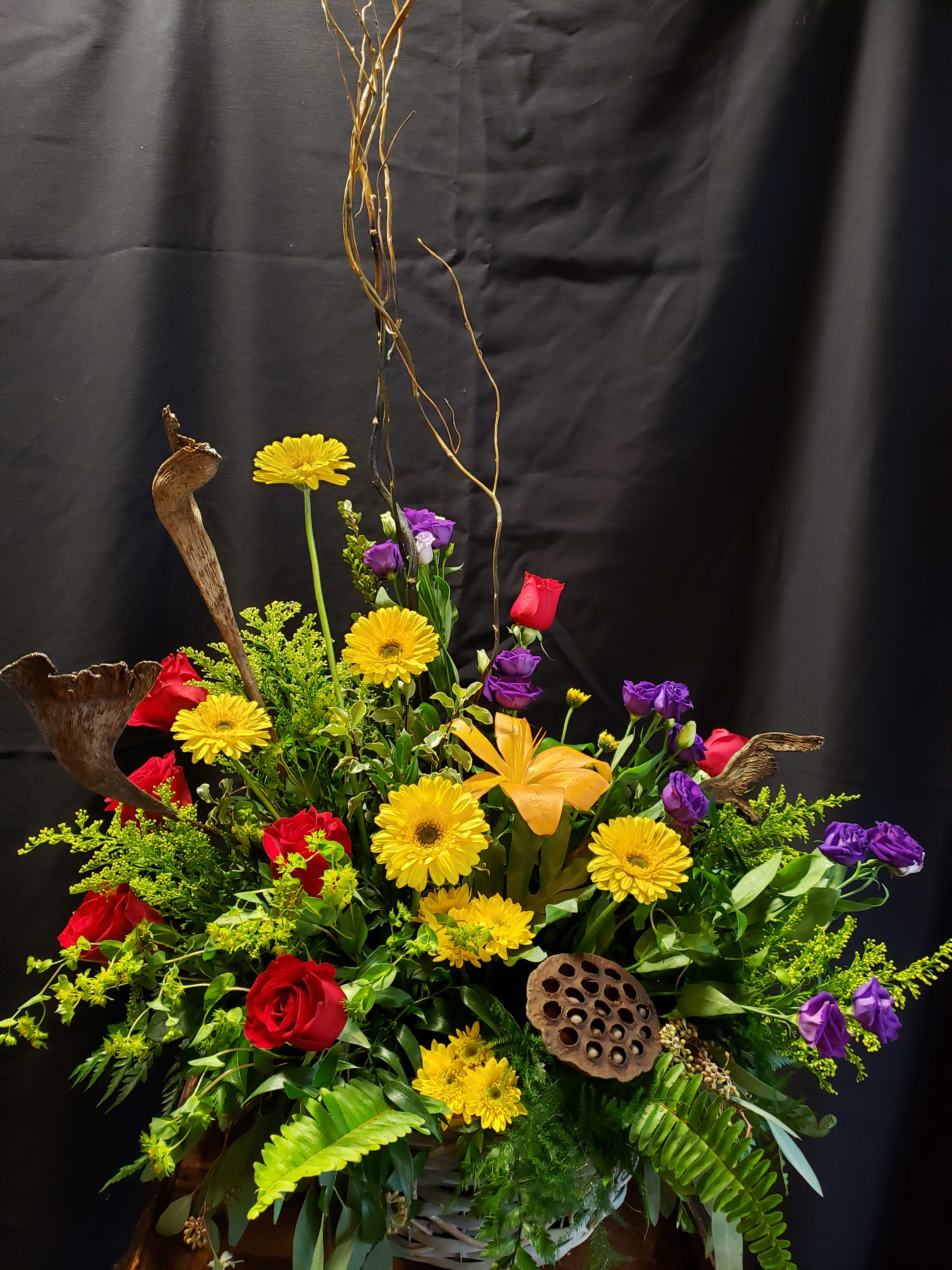 Large mixed floral arrangement with red roses, yellow daisies, and purple blooms