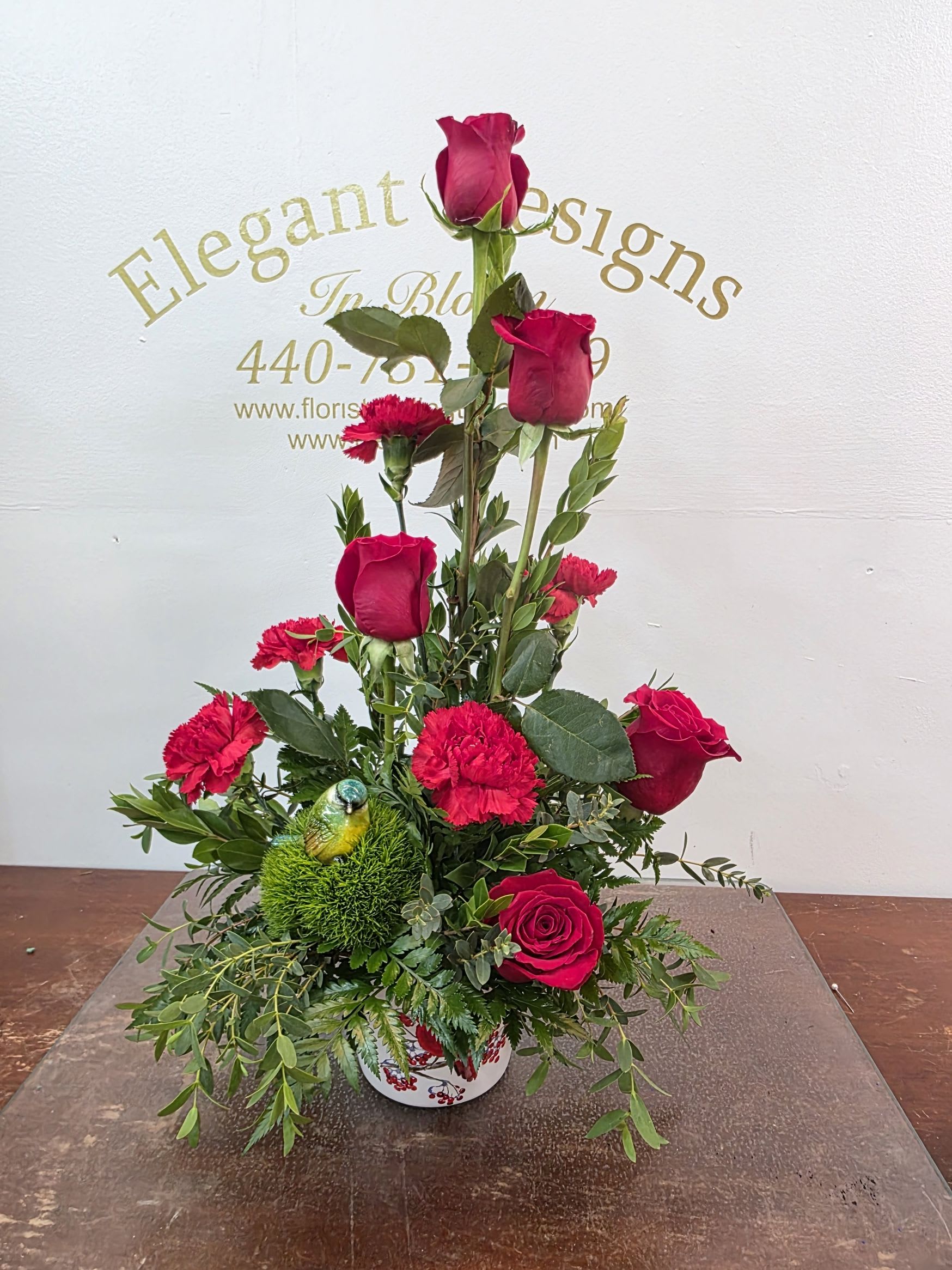 Blue Bird &amp; Cardinals - Nature is our connection to the past and each other. This sweet sentiment of the blue bird and the reminder of loved ones passed in the cardinal vase is sure to draw attention. Red carnations and roses accented with premium greenery is vibrant and alluring. For the home or a service this arrangement speaks volumes