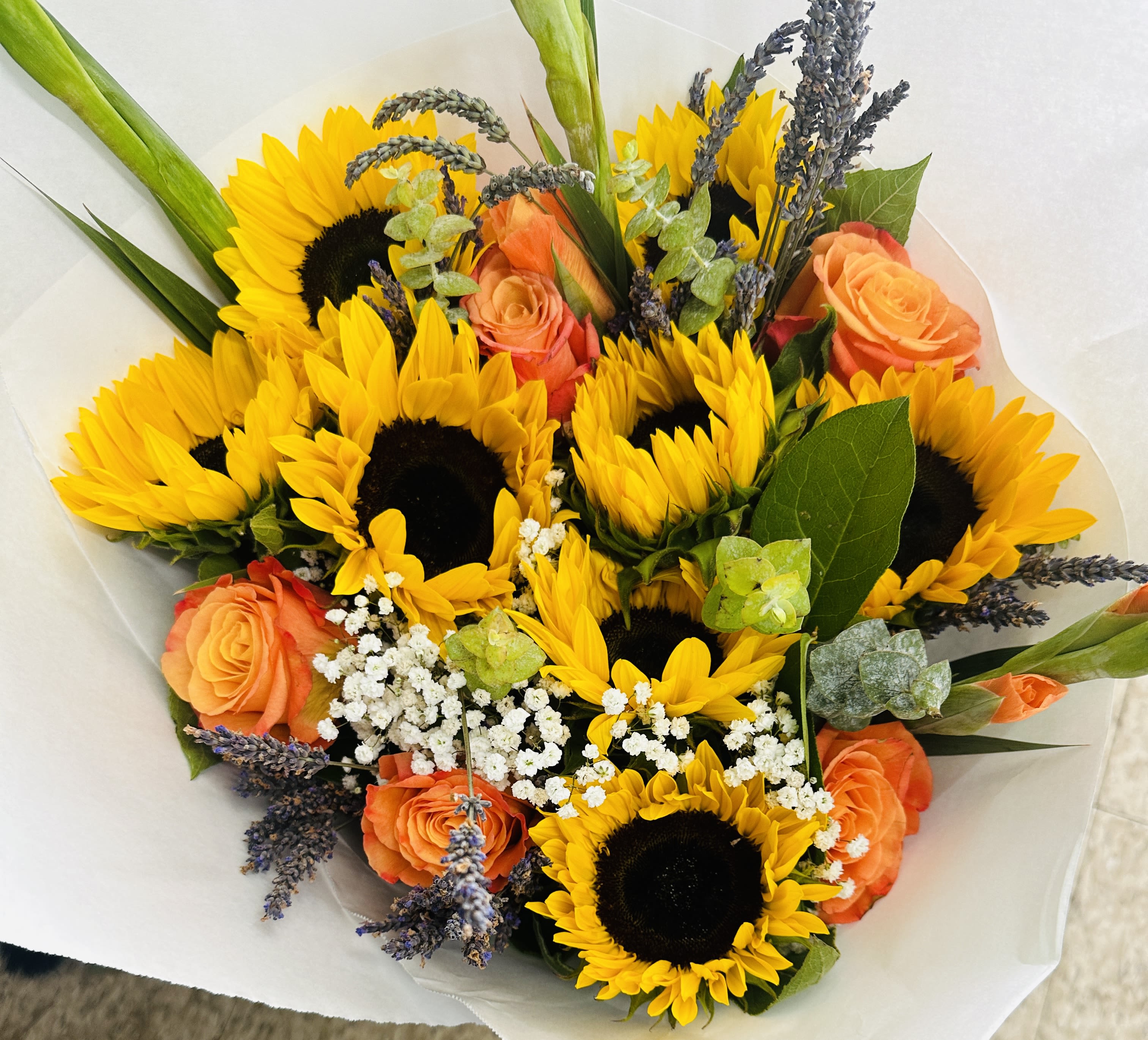 Bouquet of yellow sunflowers, orange roses, and white filler flowers wrapped in white paper