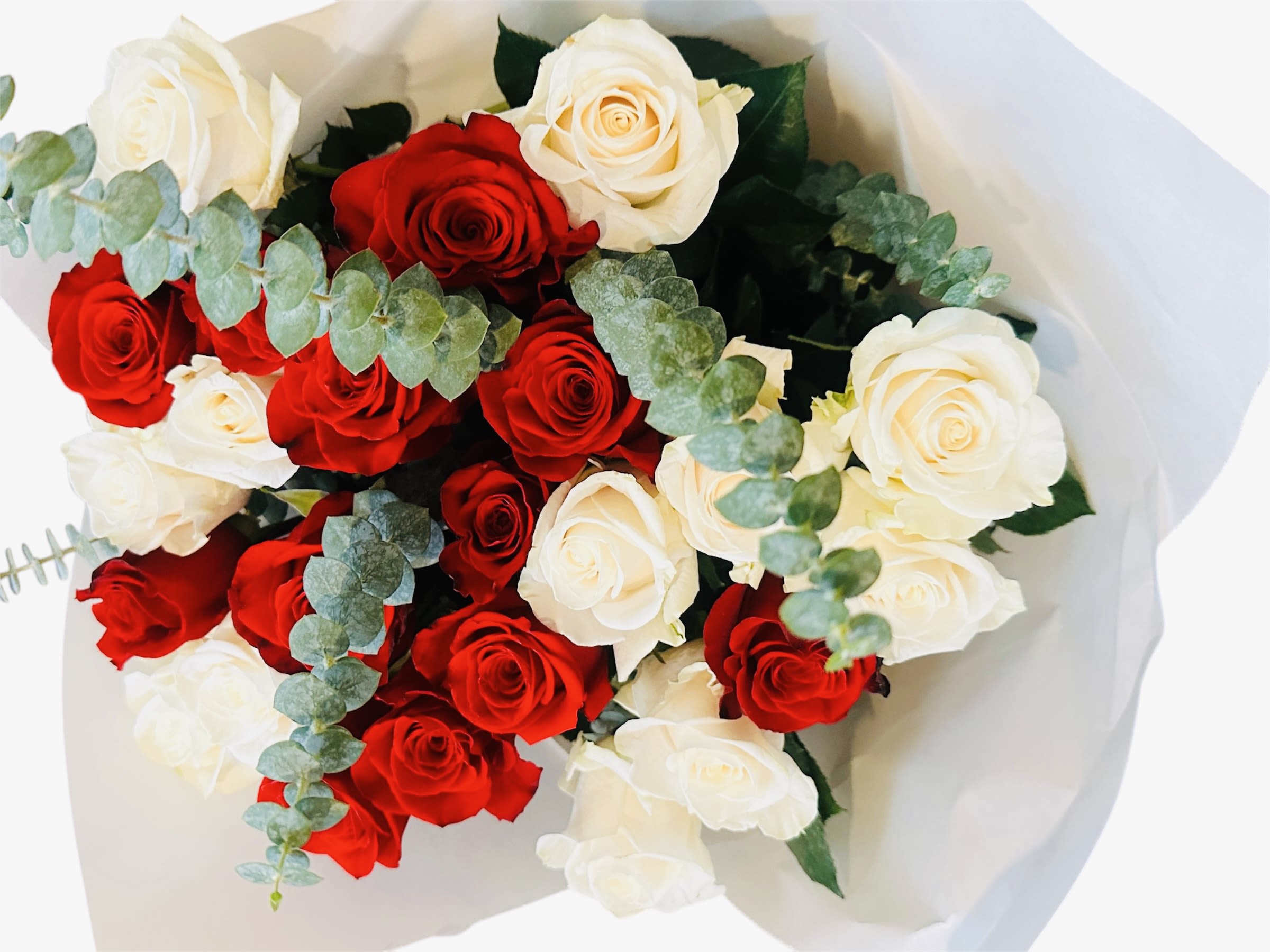 Hand-tied bouquet of red and cream roses with eucalyptus in white paper wrap