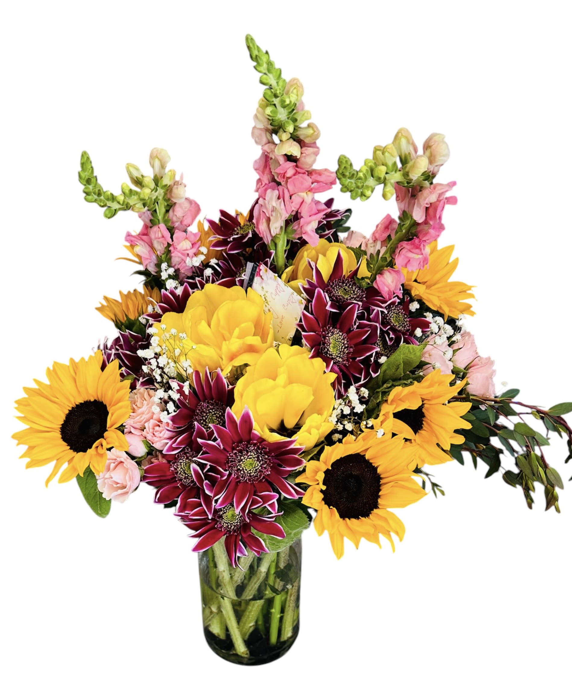 Tall mixed arrangement with sunflowers, burgundy mums, yellow blooms and pink snapdragons in a clear glass vase