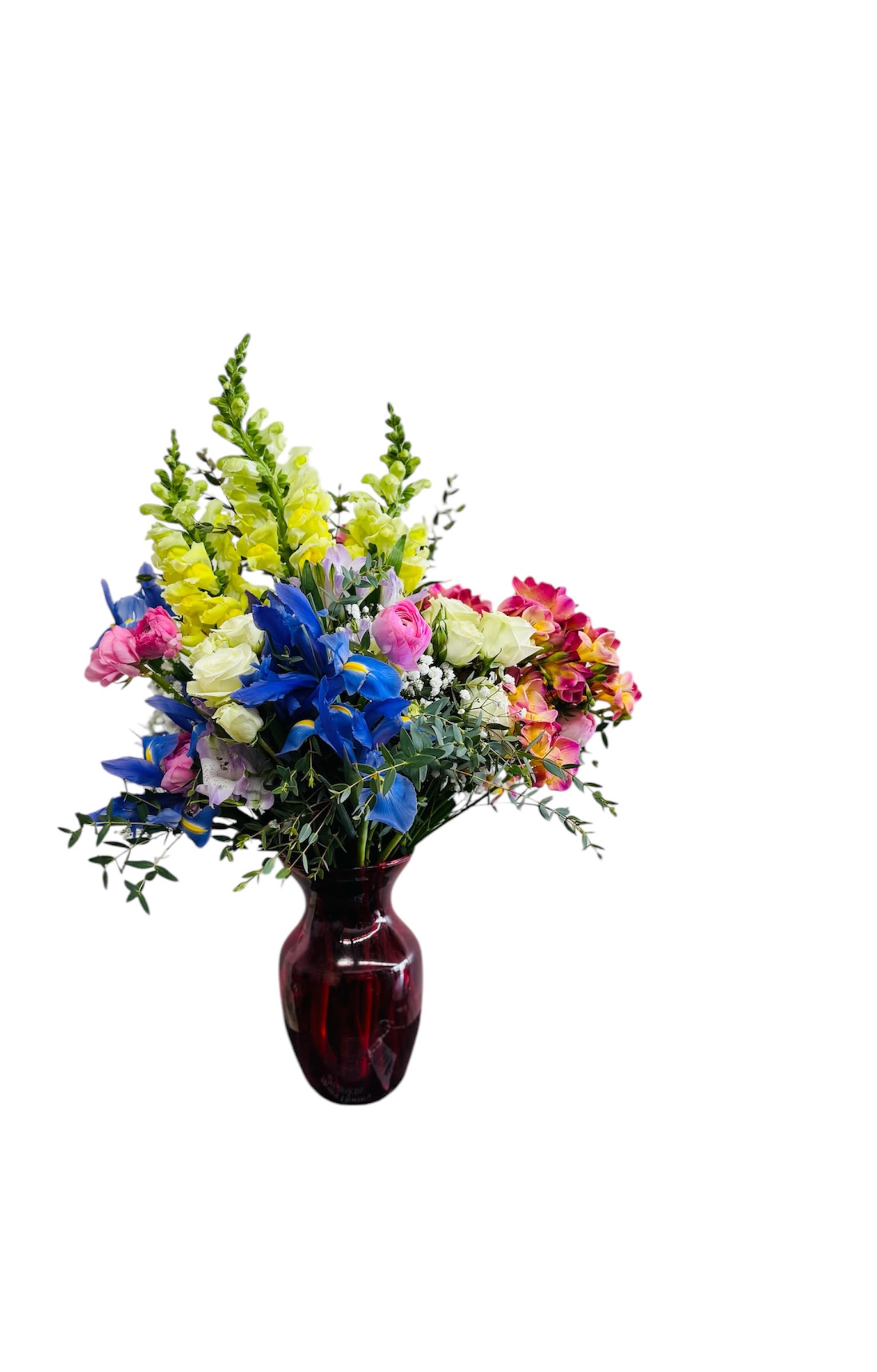 Tall mixed arrangement of yellow snapdragons, blue iris, and pink roses in a dark red glass vase.