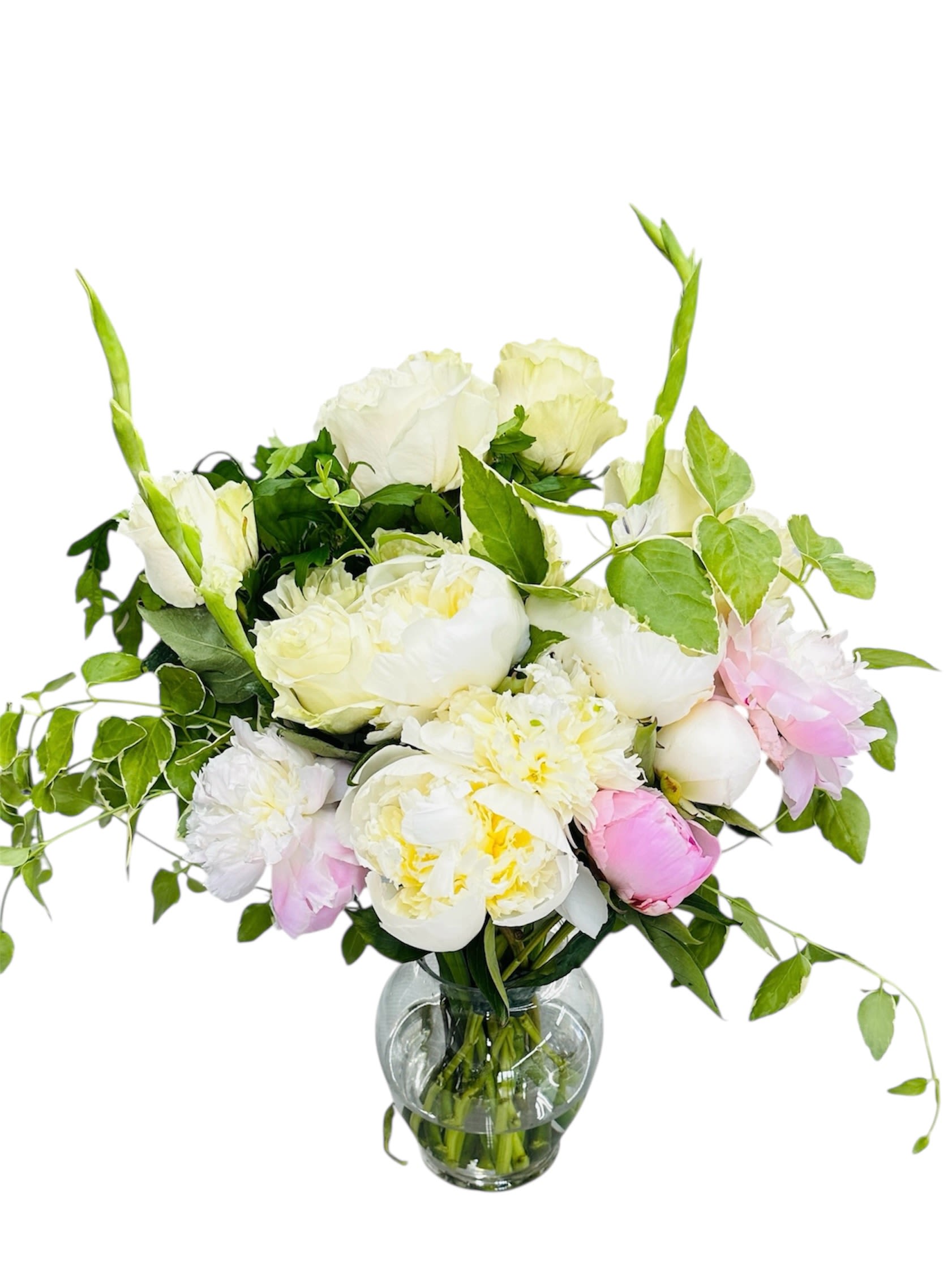 White and blush peony and rose arrangement with trailing vines in a clear glass vase