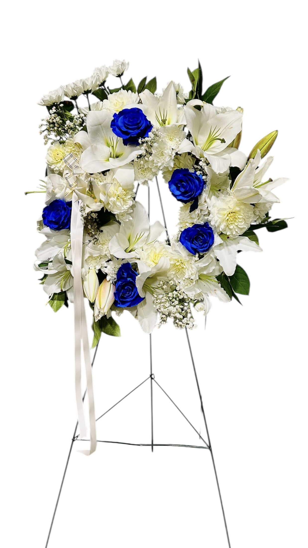 Standing wreath of white lilies and bright blue roses on a metal easel with white ribbon
