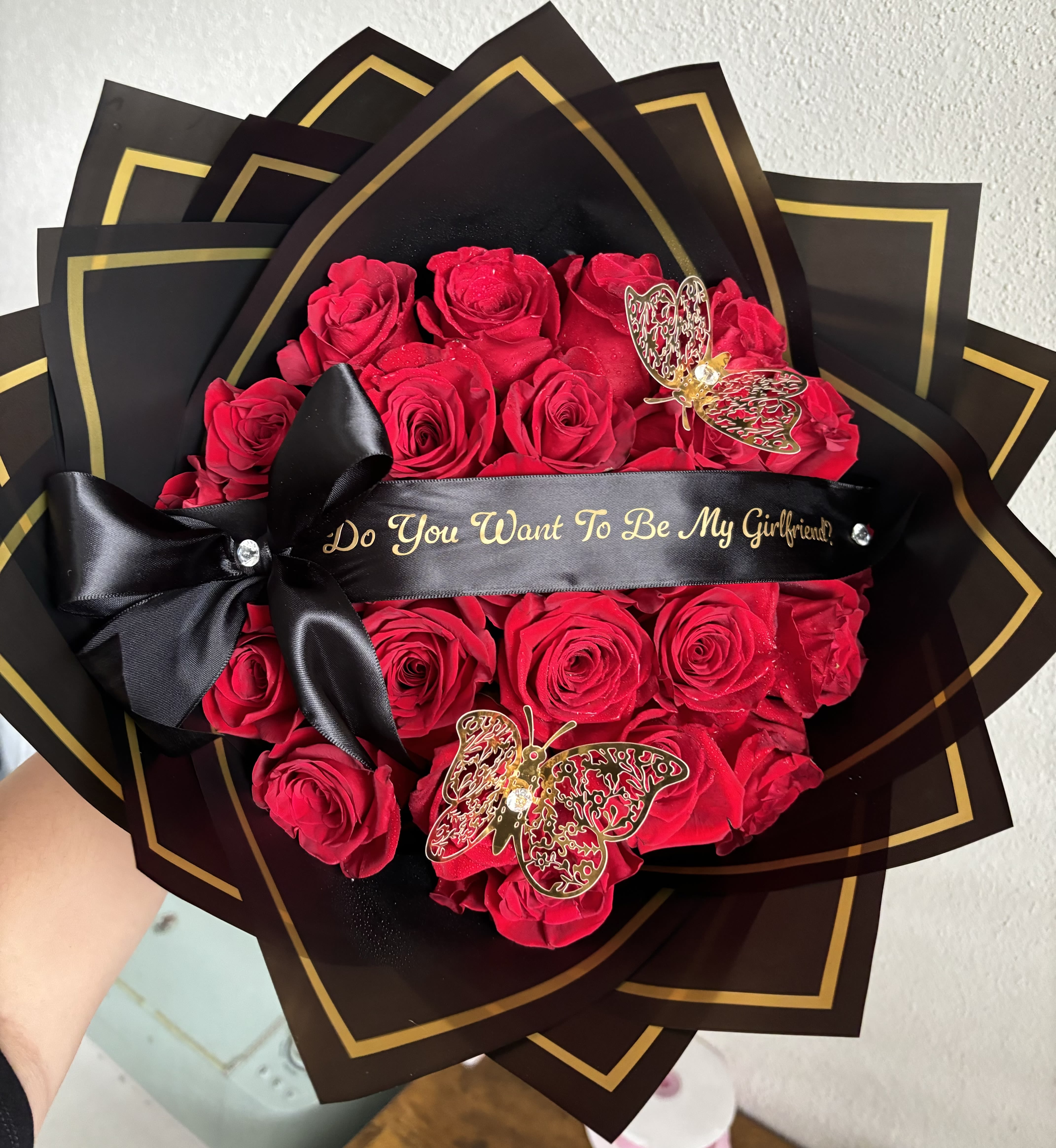 Red roses wrapped in black paper with gold trim and a black ribbon