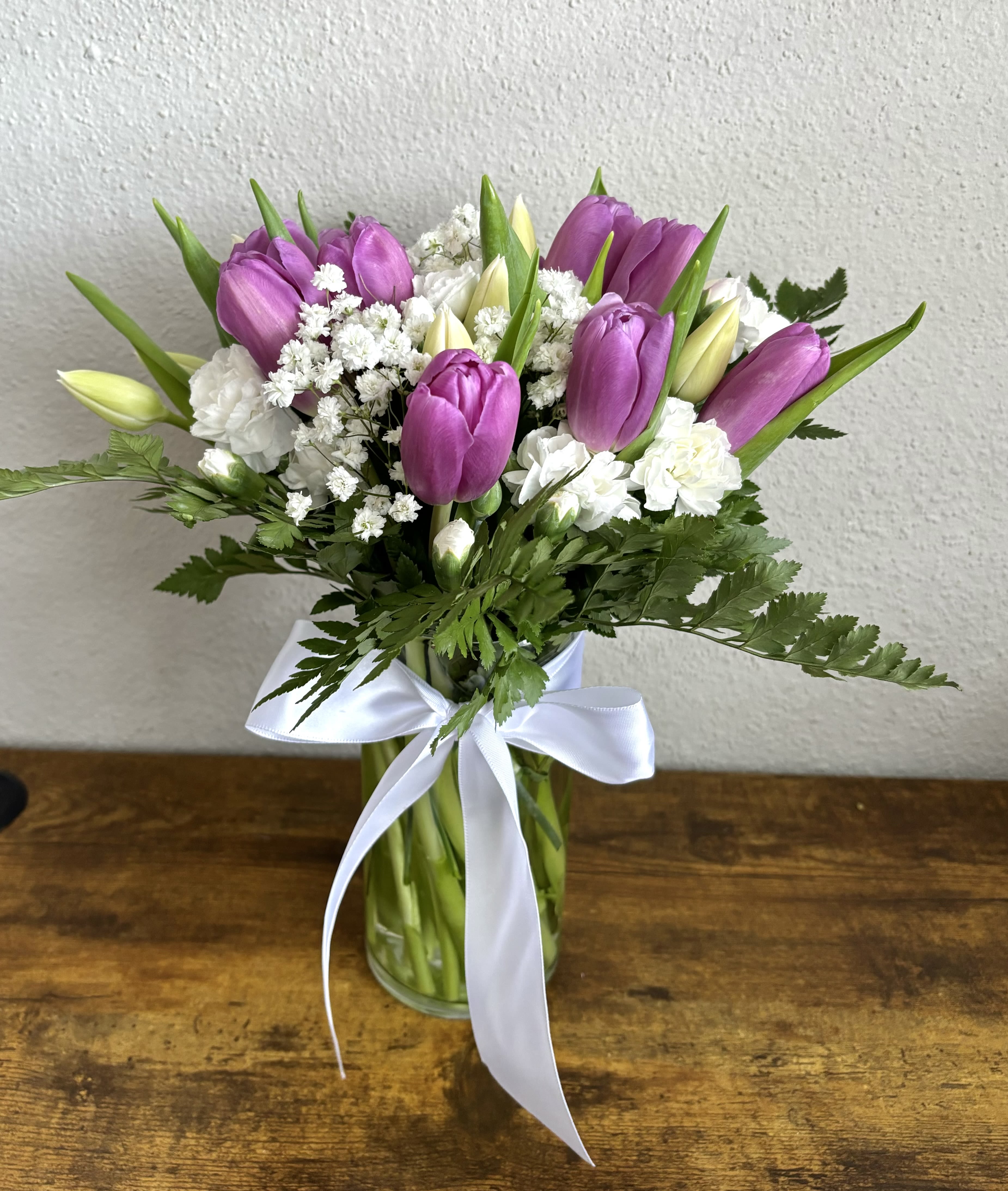 Bouquet of purple tulips and white flowers in a glass vase with a white ribbon