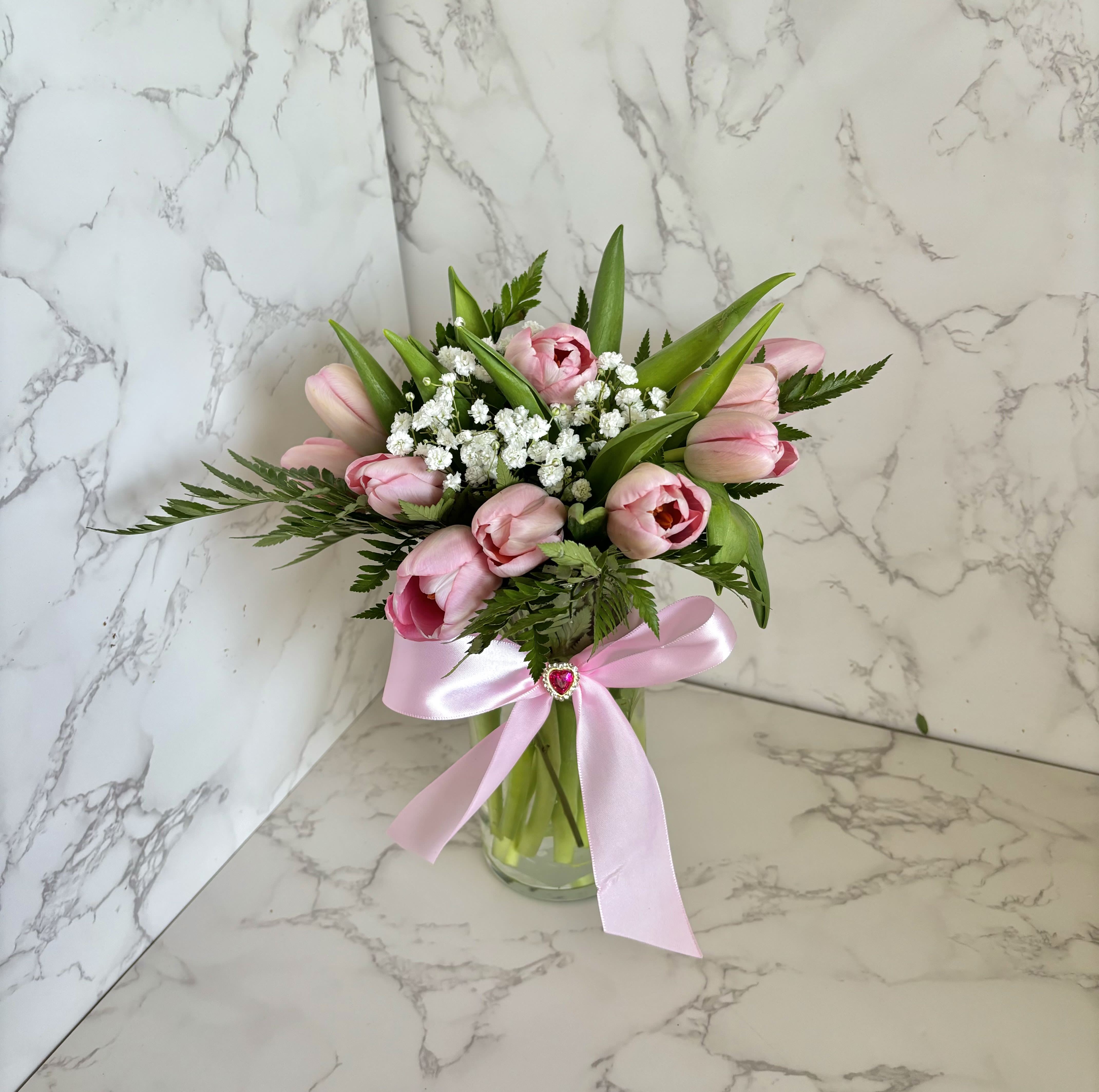 Pink tulips and white filler flowers in a glass vase with a pink ribbon