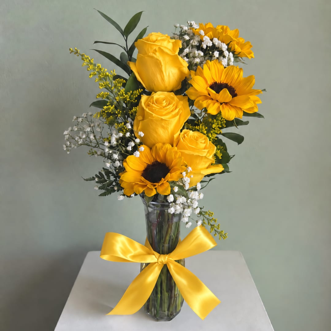 Yellow roses and sunflowers in a clear glass vase with a yellow ribbon