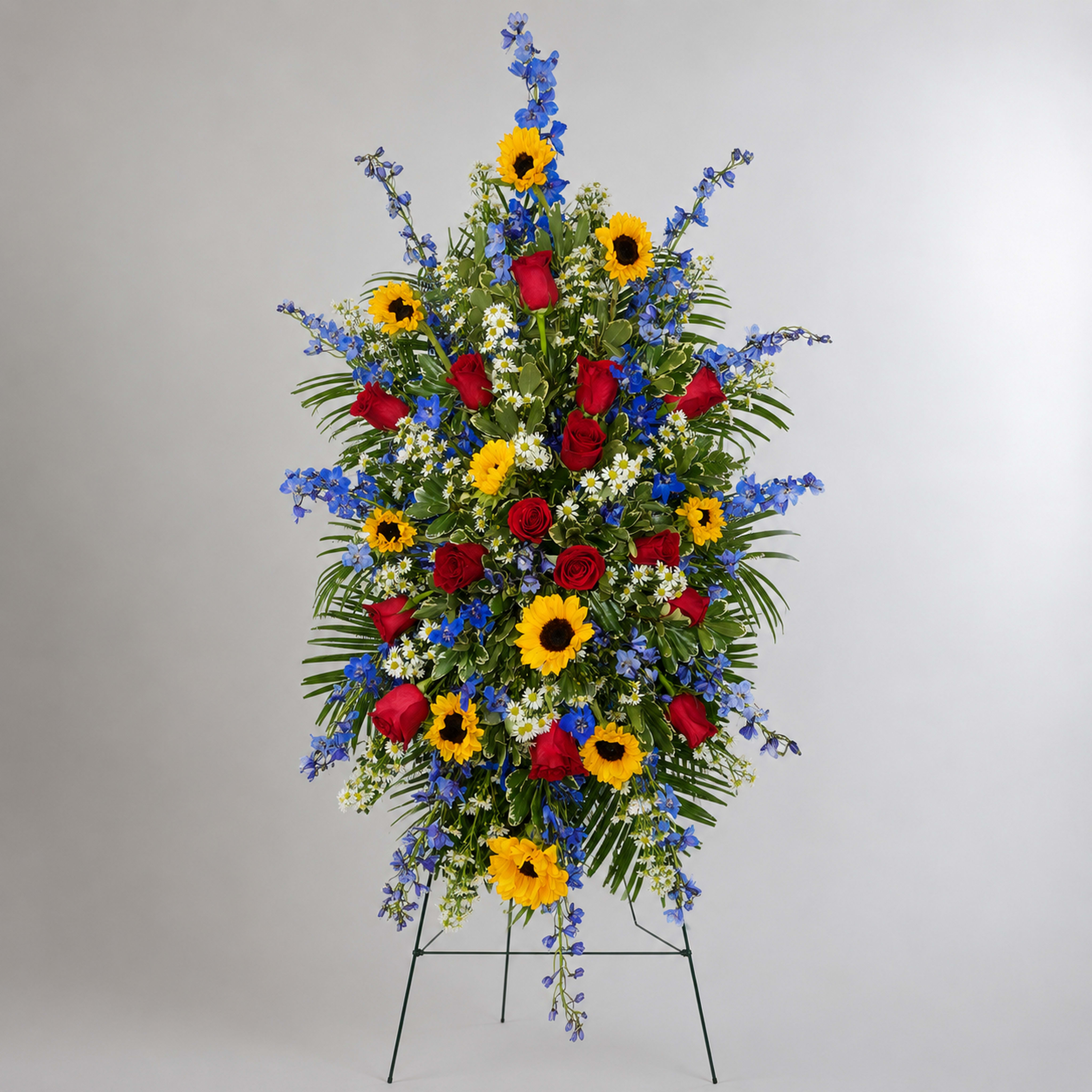 Standing floral spray with red roses, sunflowers, and blue flowers on a metal easel