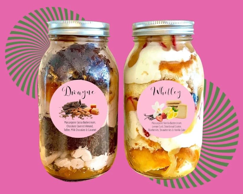 Two dessert jars with layered cake and frosting on a pink background