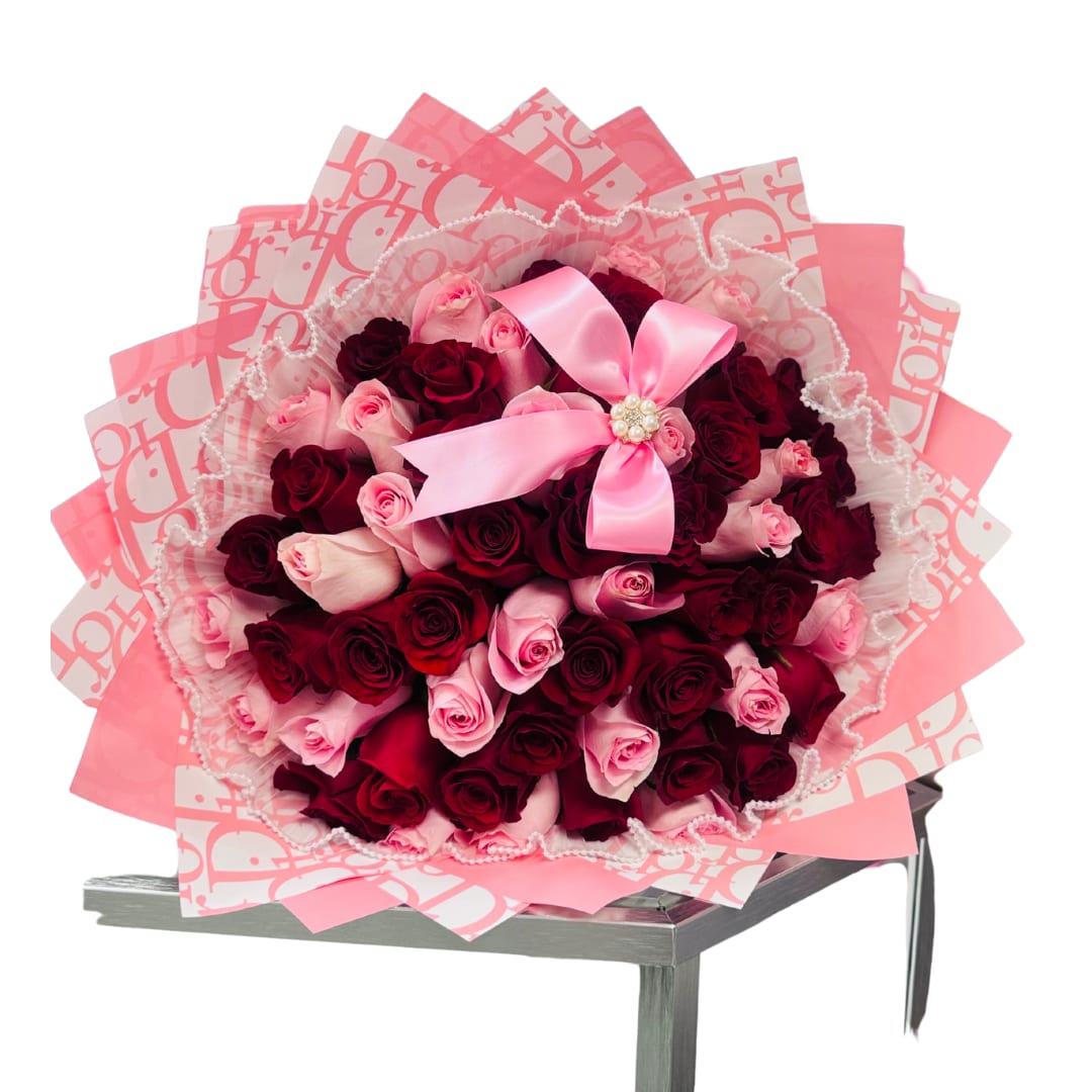 Large bouquet of red and pink roses wrapped in layered pink paper with lace trim and a pink bow.