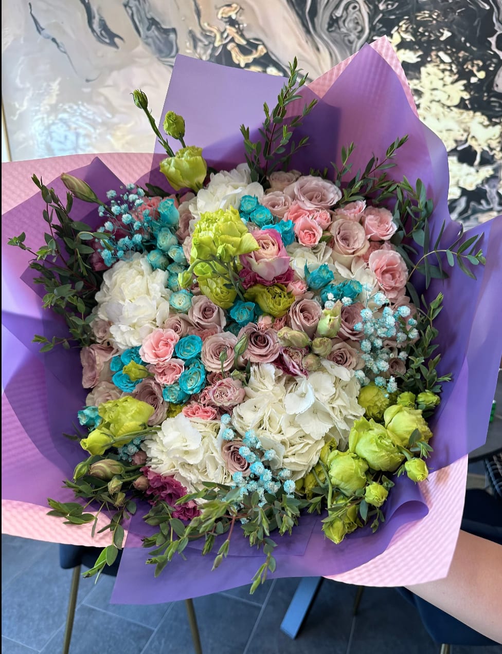 Bouquet of pastel roses, hydrangeas, and green lisianthus wrapped in purple paper