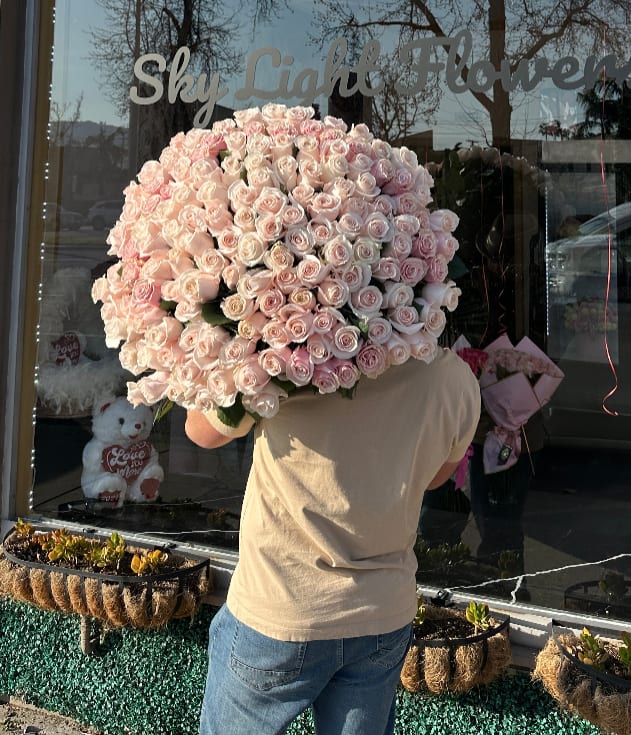 Large bouquet of pale pink roses held in front of a shop window