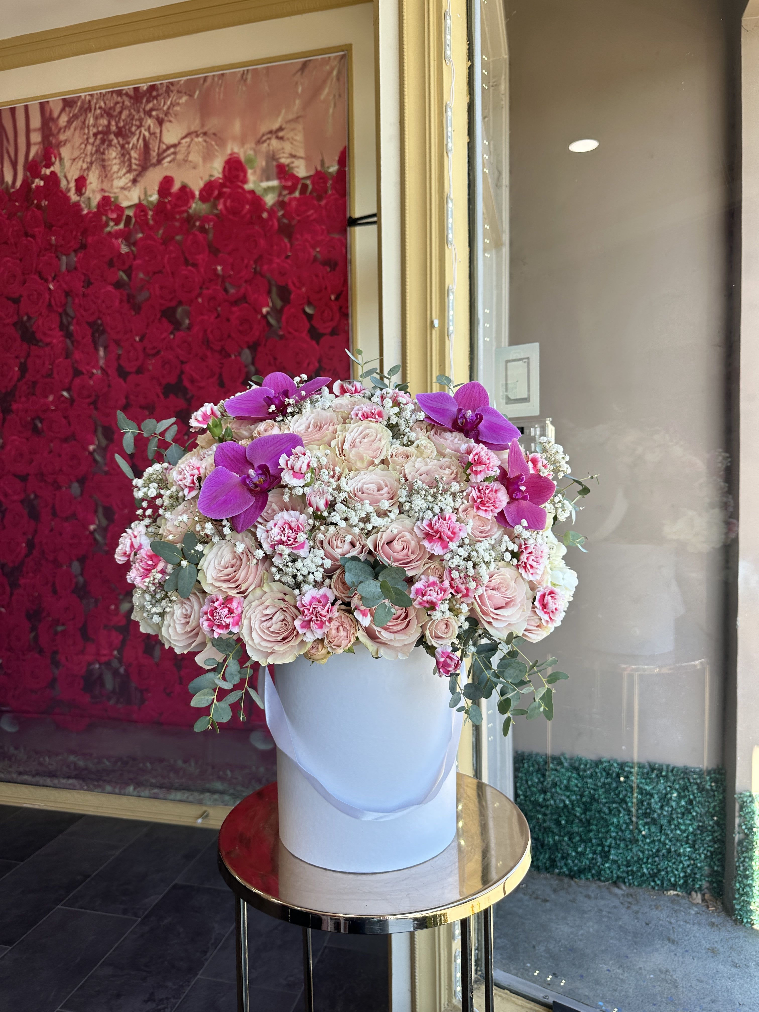 Large pink rose arrangement in a white hatbox with purple orchids