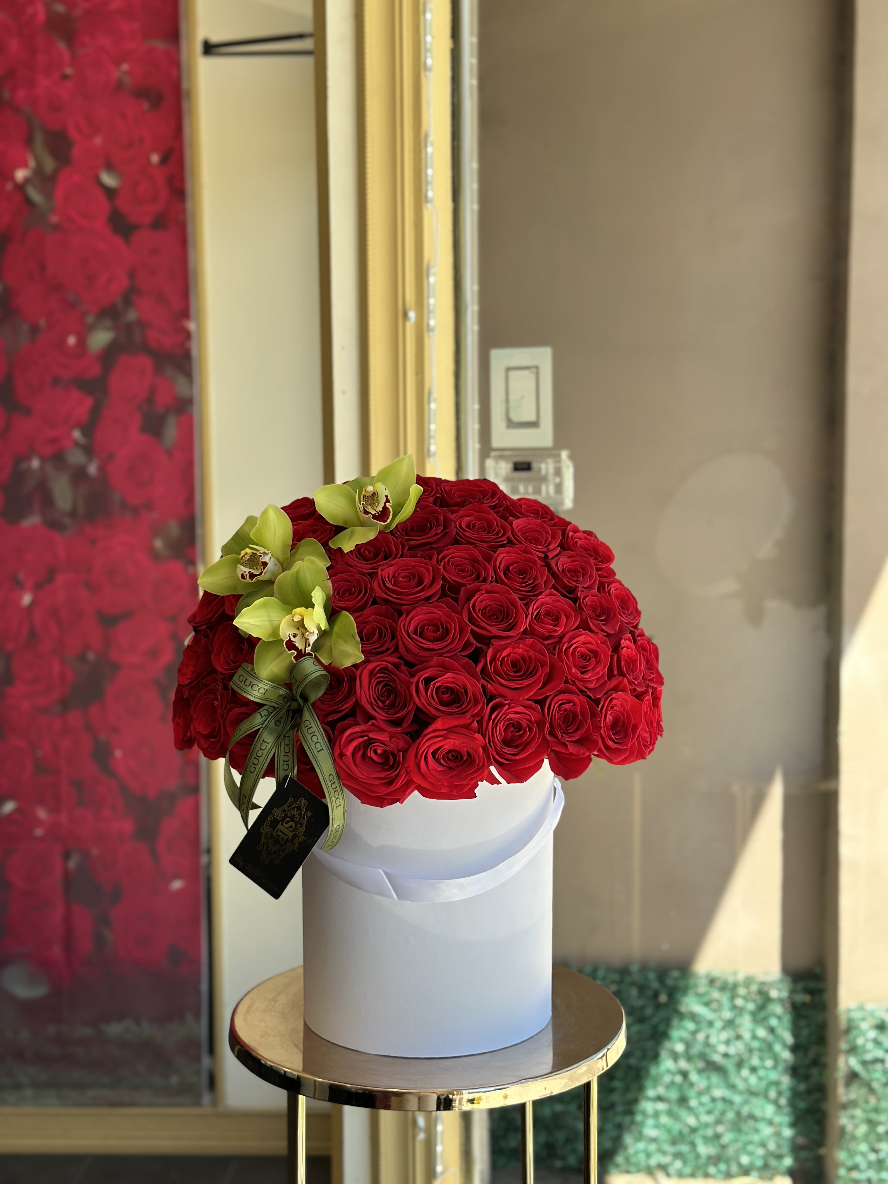 Round bouquet of red roses with green orchids in a white box