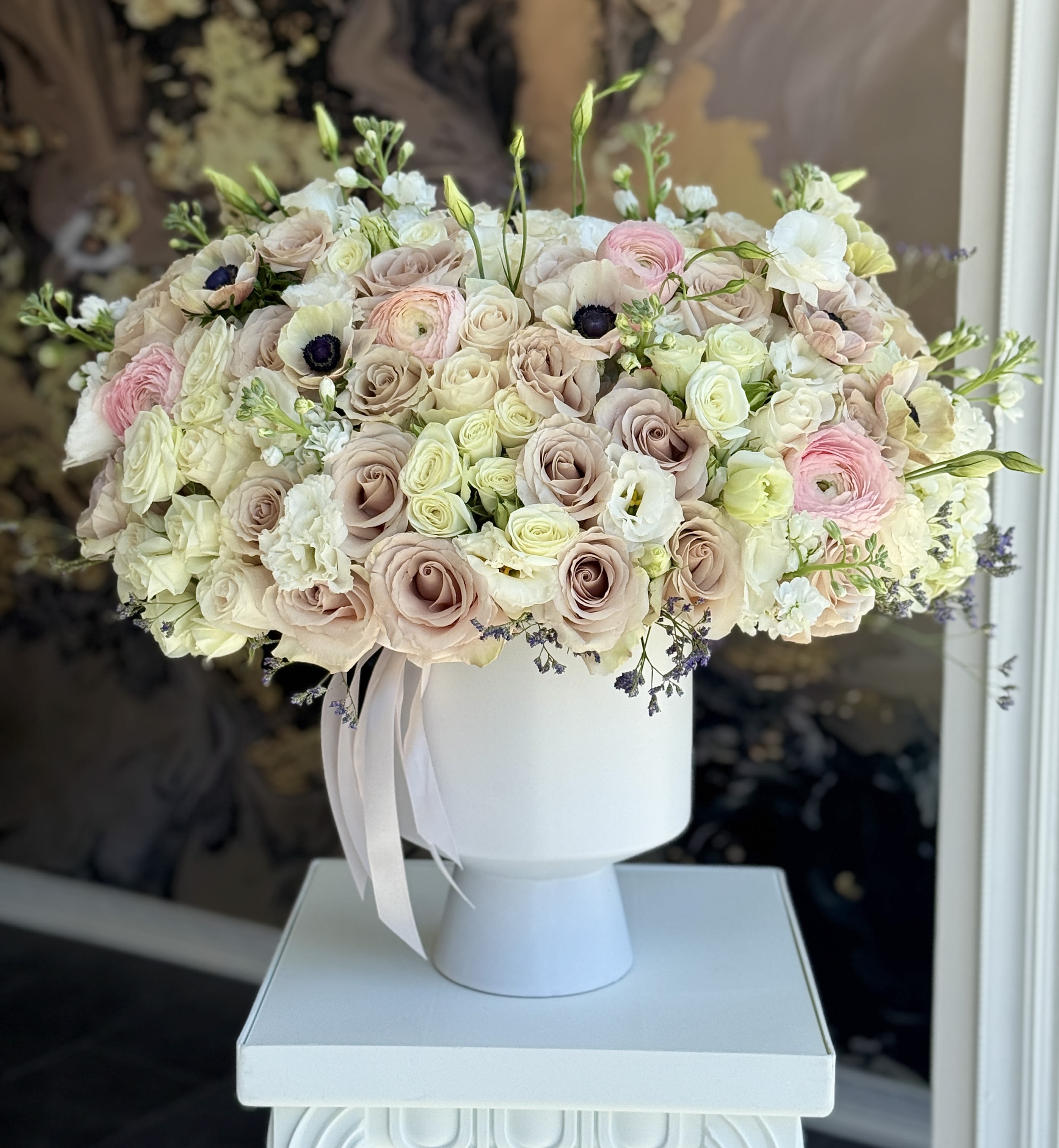 Blush and white rose arrangement in a white pedestal vase