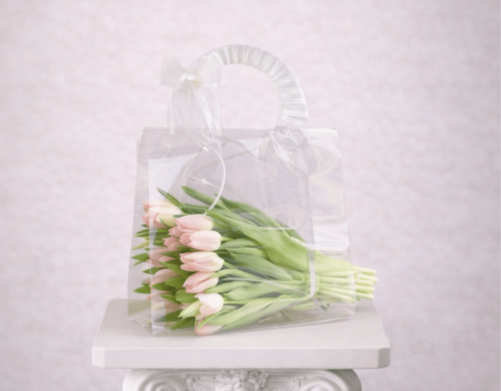 A wrapped bouquet of pale pink tulips in a clear gift bag