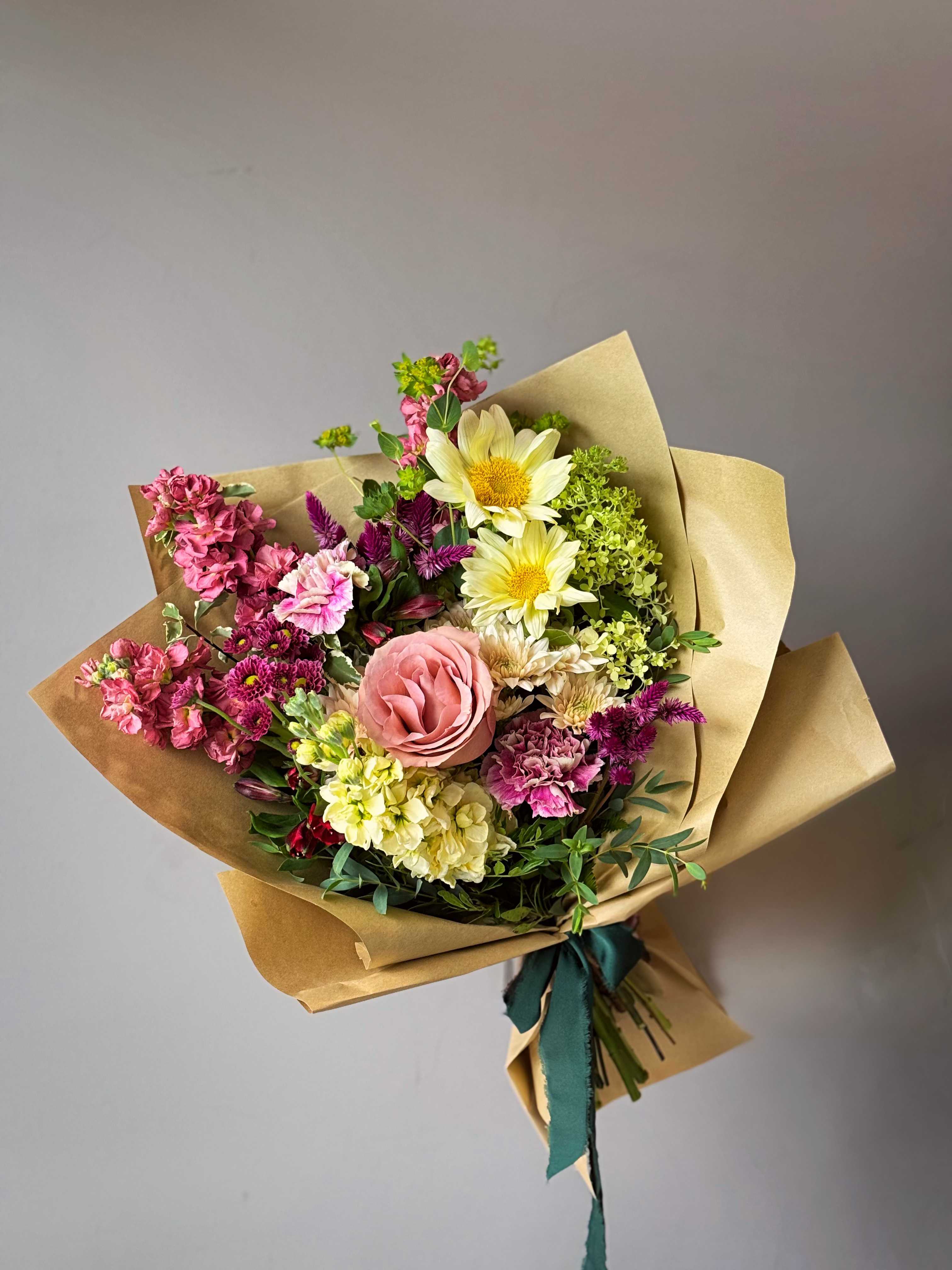 Hand-tied bouquet of pink, yellow, and purple flowers in kraft paper