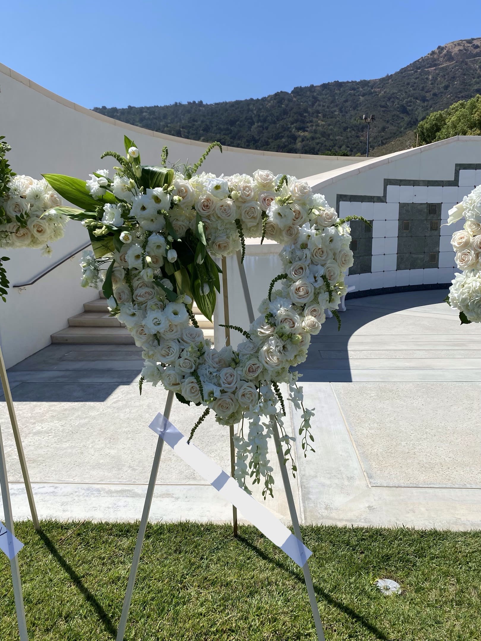 Heavenly Clouds =  Santa Clarita Valley Florist - An all white tribute, this white Heart funeral spray is pure and tranquil. Featuring a variety of white flowers, this elegant easel compliments the beauty of life.