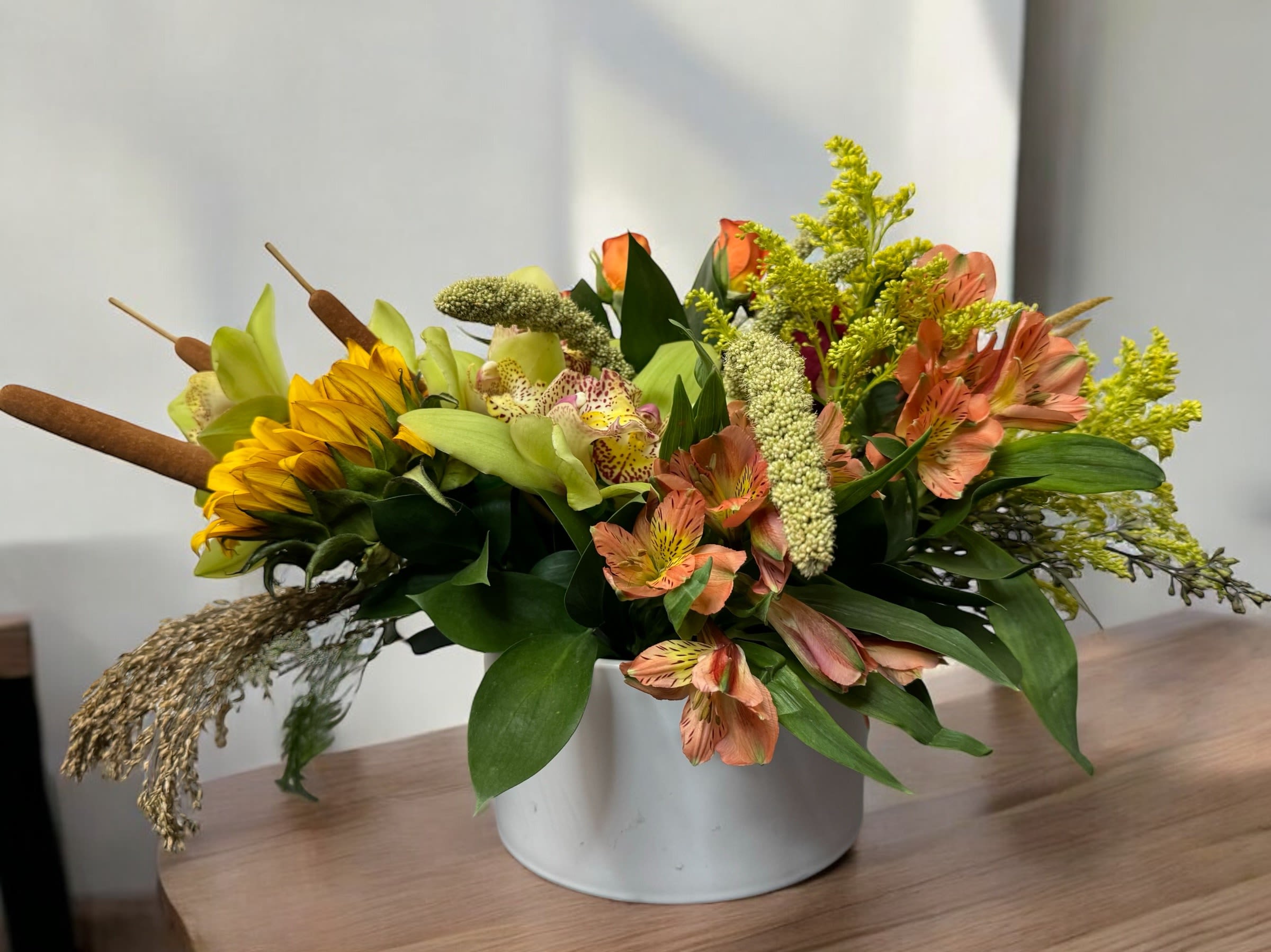 Mixed floral arrangement in a white container with yellow and peach blooms