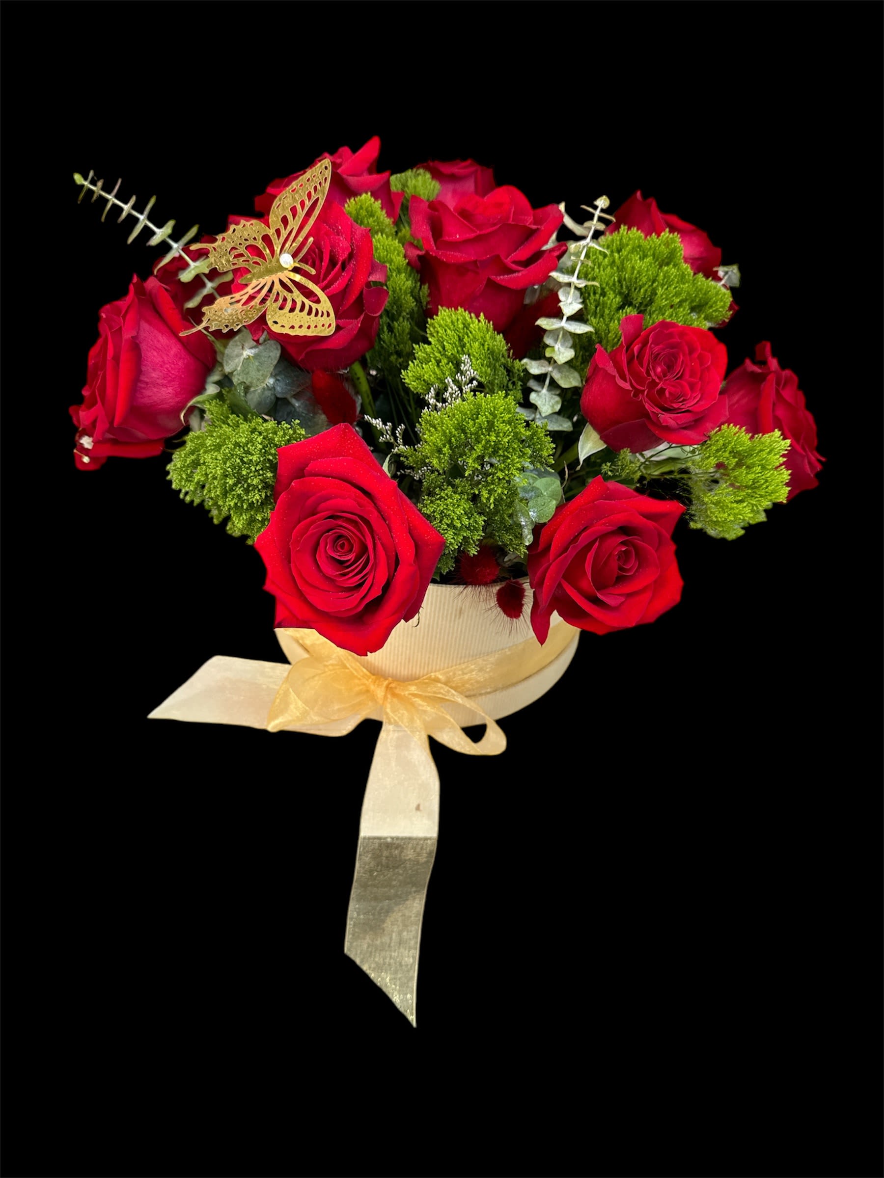 Red roses arranged in a round box with a gold ribbon and butterfly accent