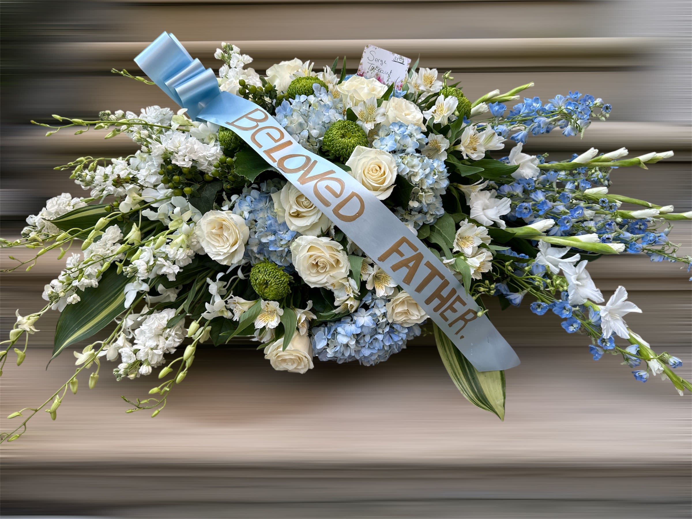 Sympathy spray of white and blue flowers with a "Beloved Father" ribbon