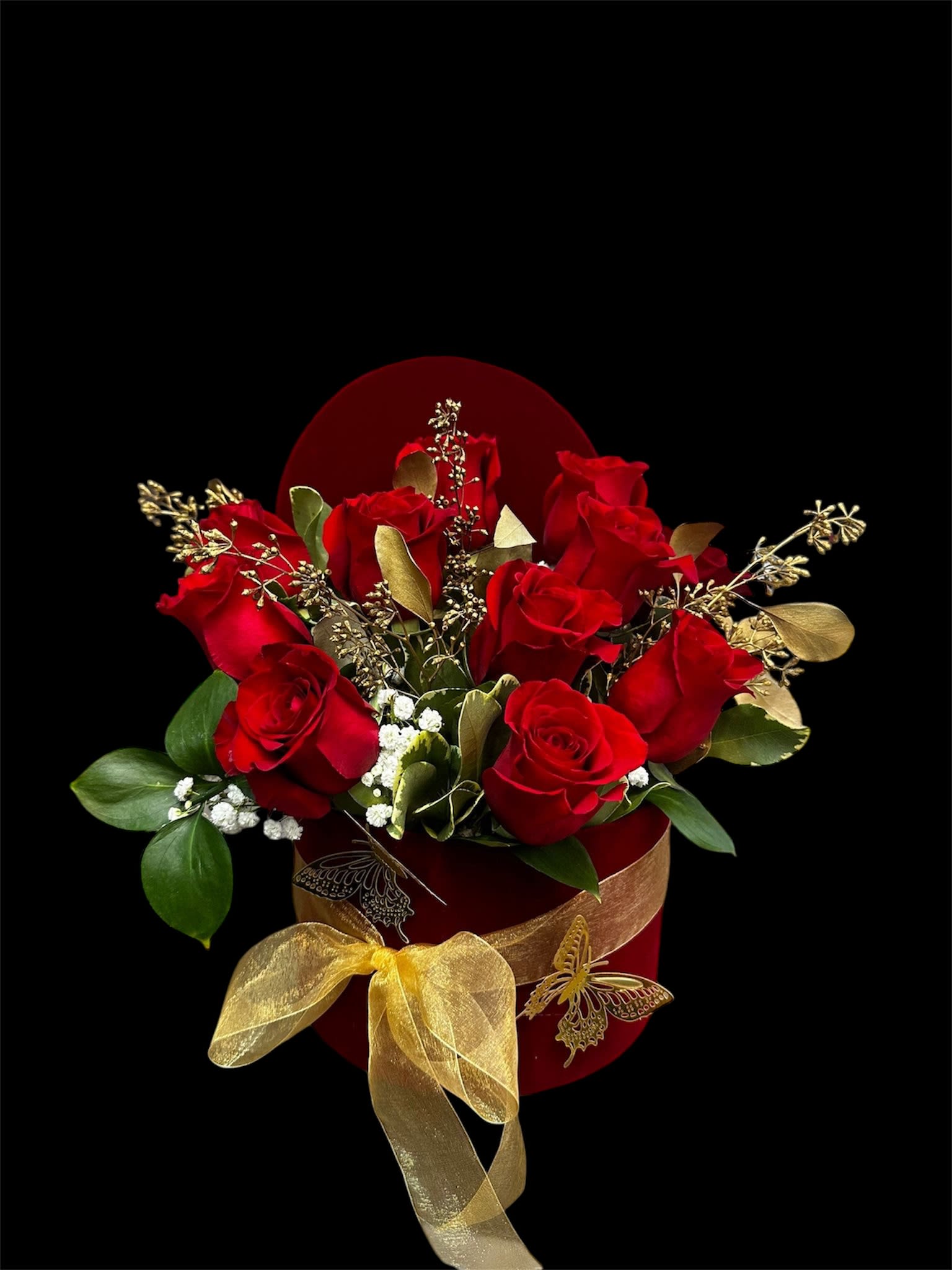 Red roses arranged in a red box with a gold ribbon