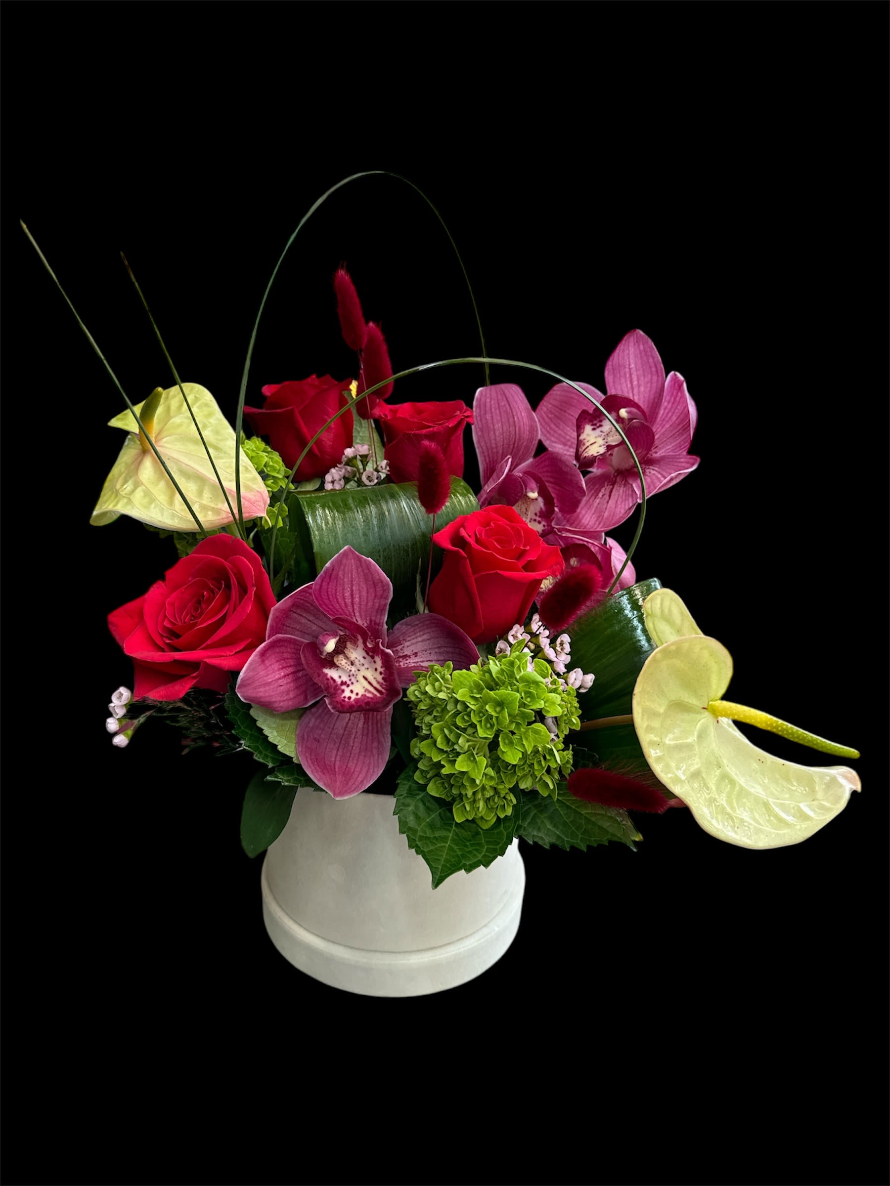 Arrangement of red roses, purple orchids, and pale anthuriums in a white vase