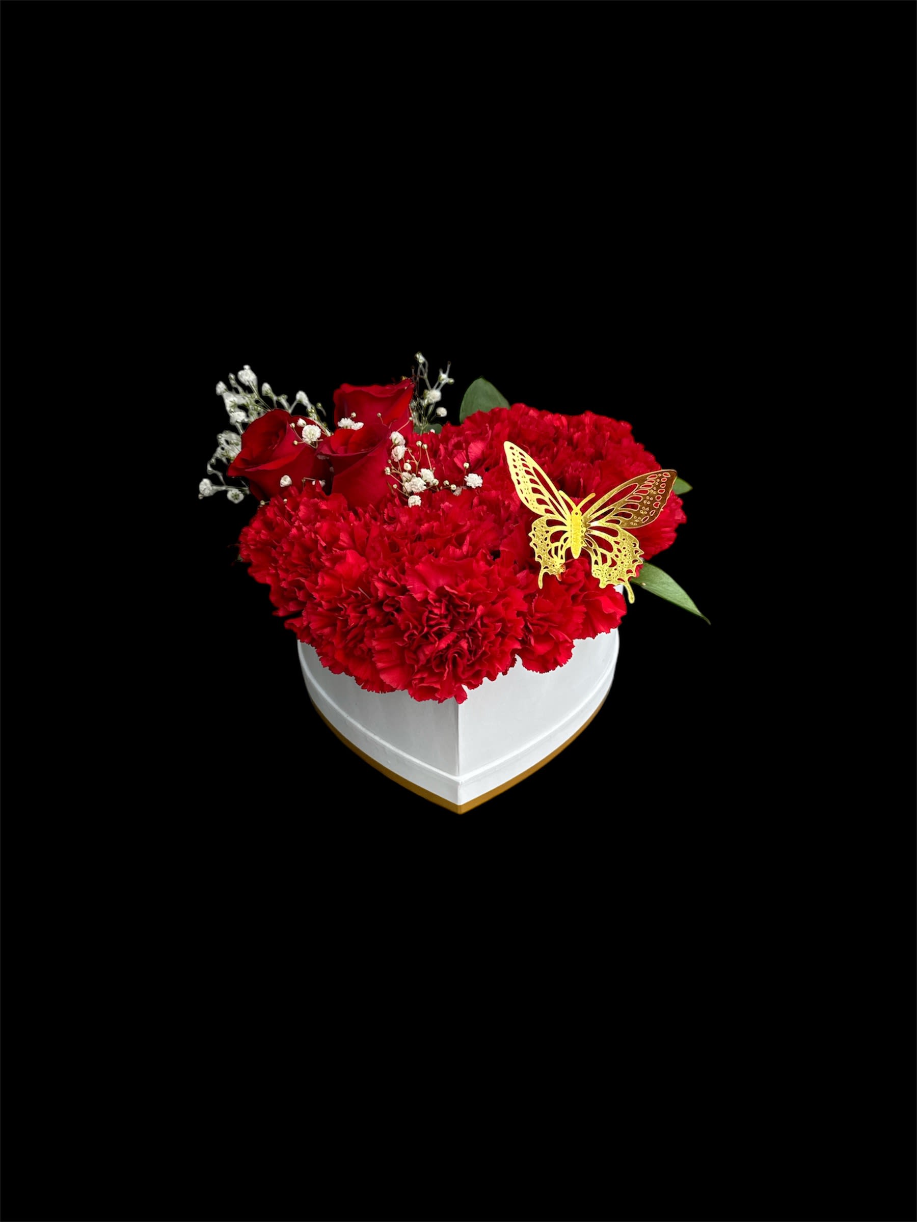 Red carnations and roses in a white heart-shaped box with a butterfly accent