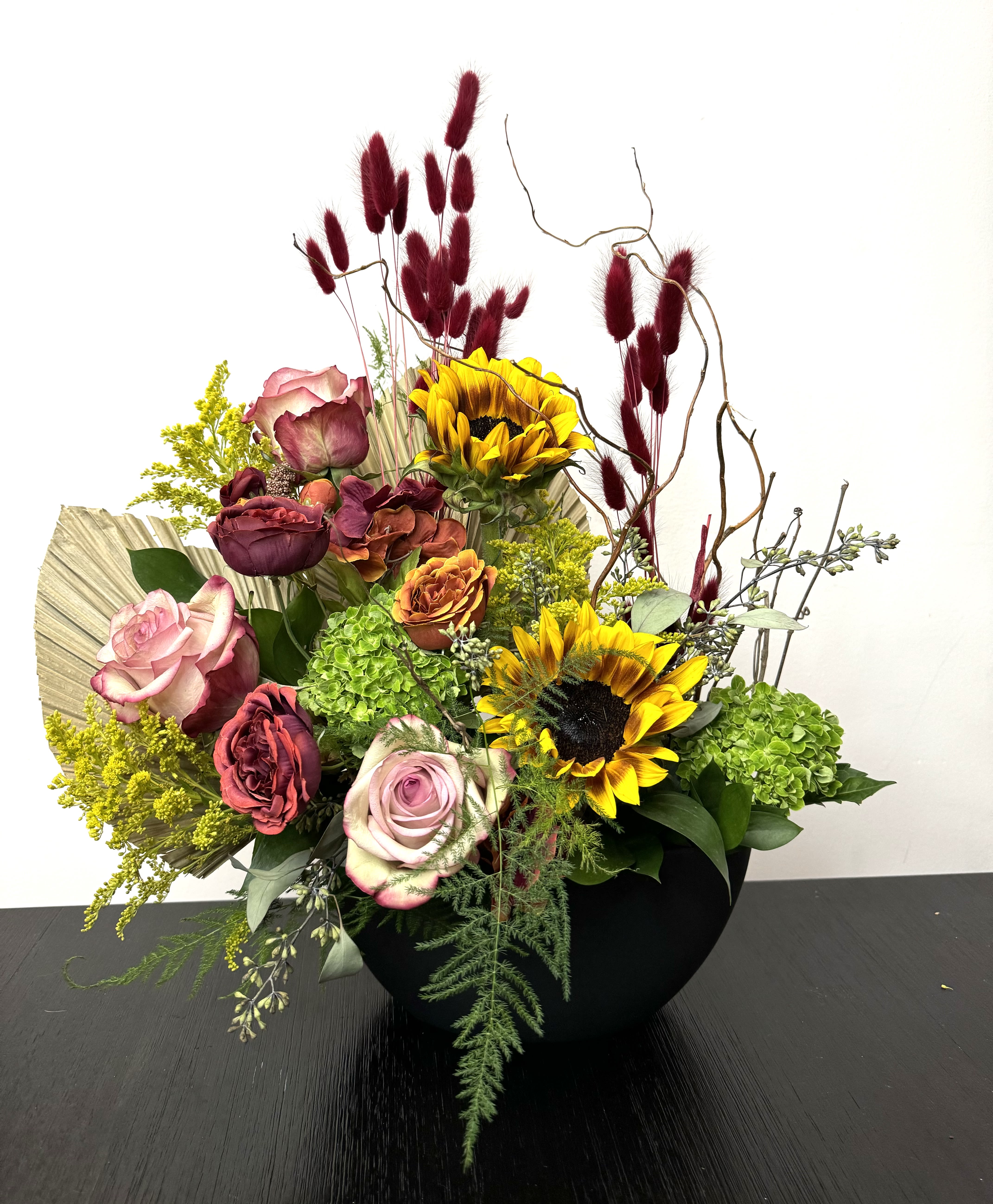 Mixed bouquet with roses, sunflowers, and green hydrangeas in a black vase