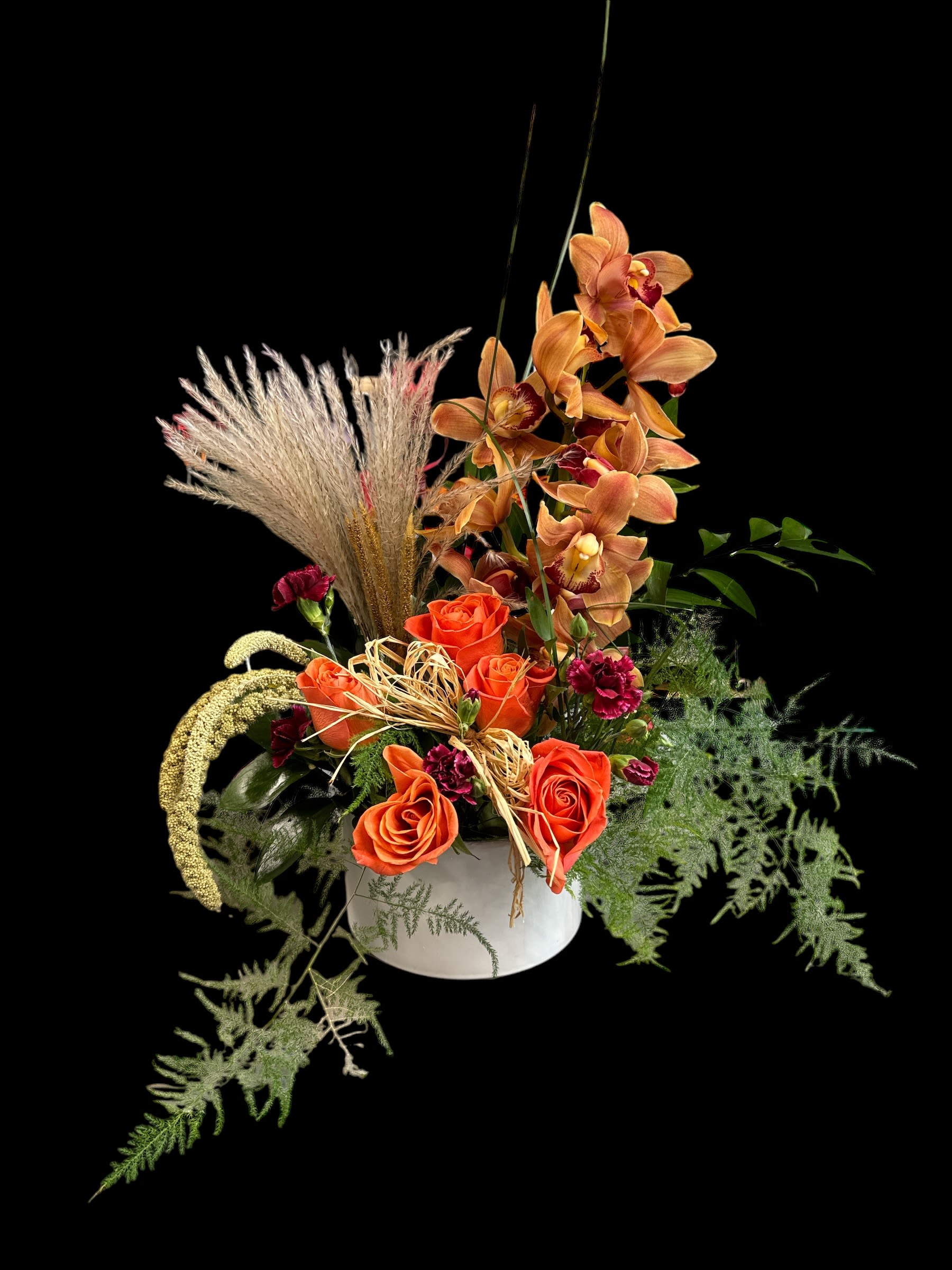 Orange roses and orchids in a white vase with dried grasses