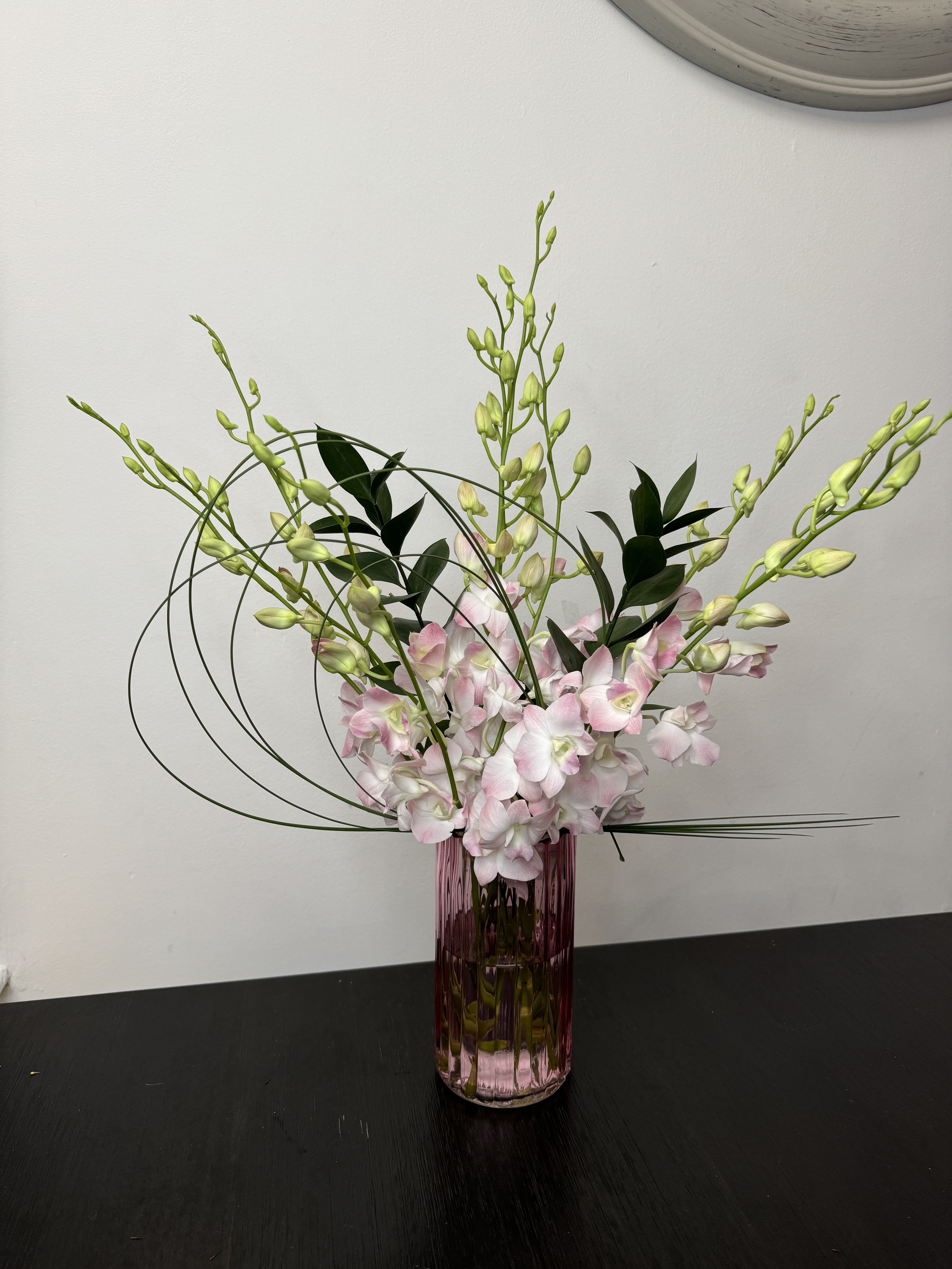 Pink orchid arrangement in a tall purple glass vase