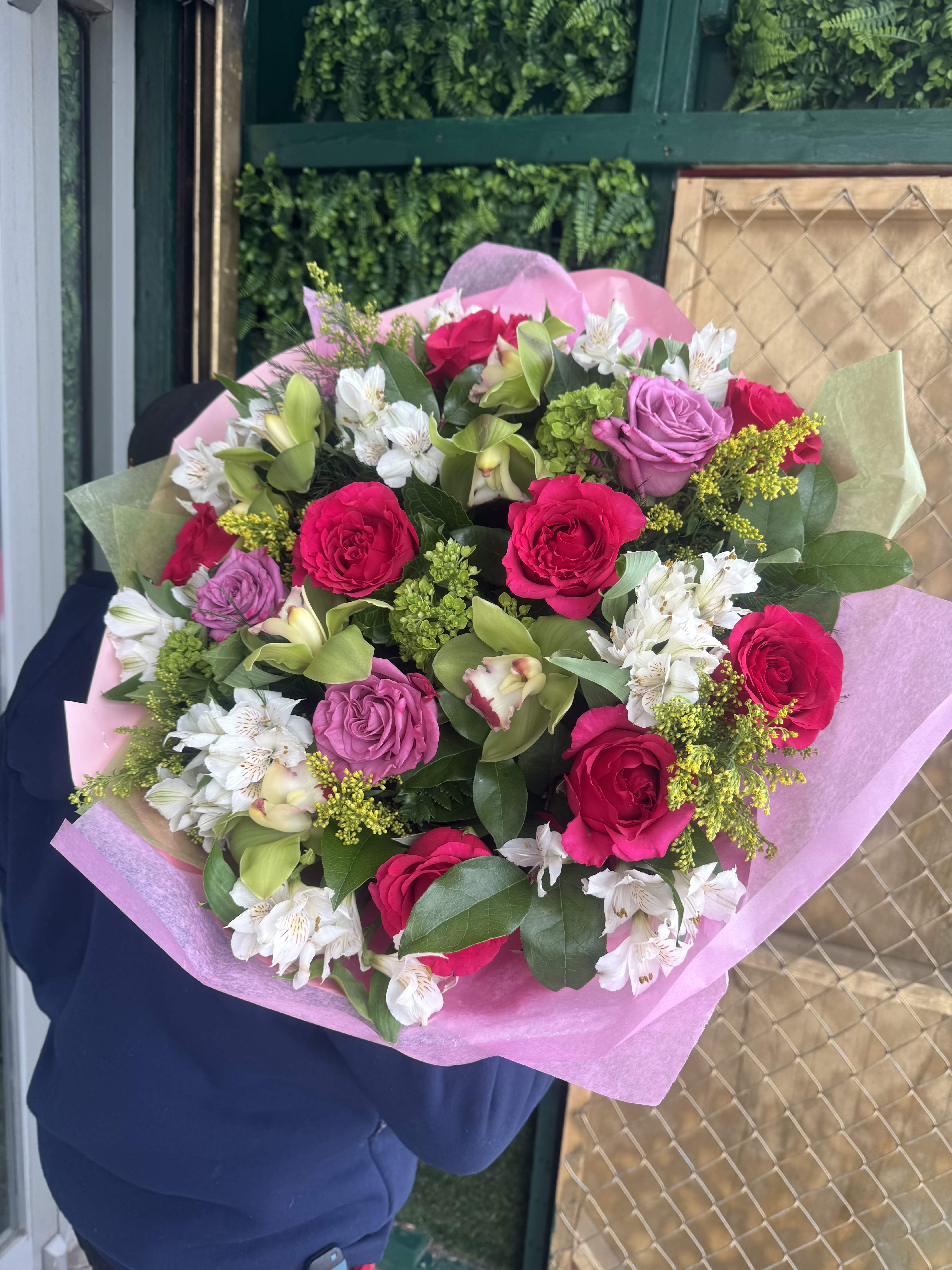 Bouquet of pink roses, white alstroemeria, and green orchids wrapped in pink paper