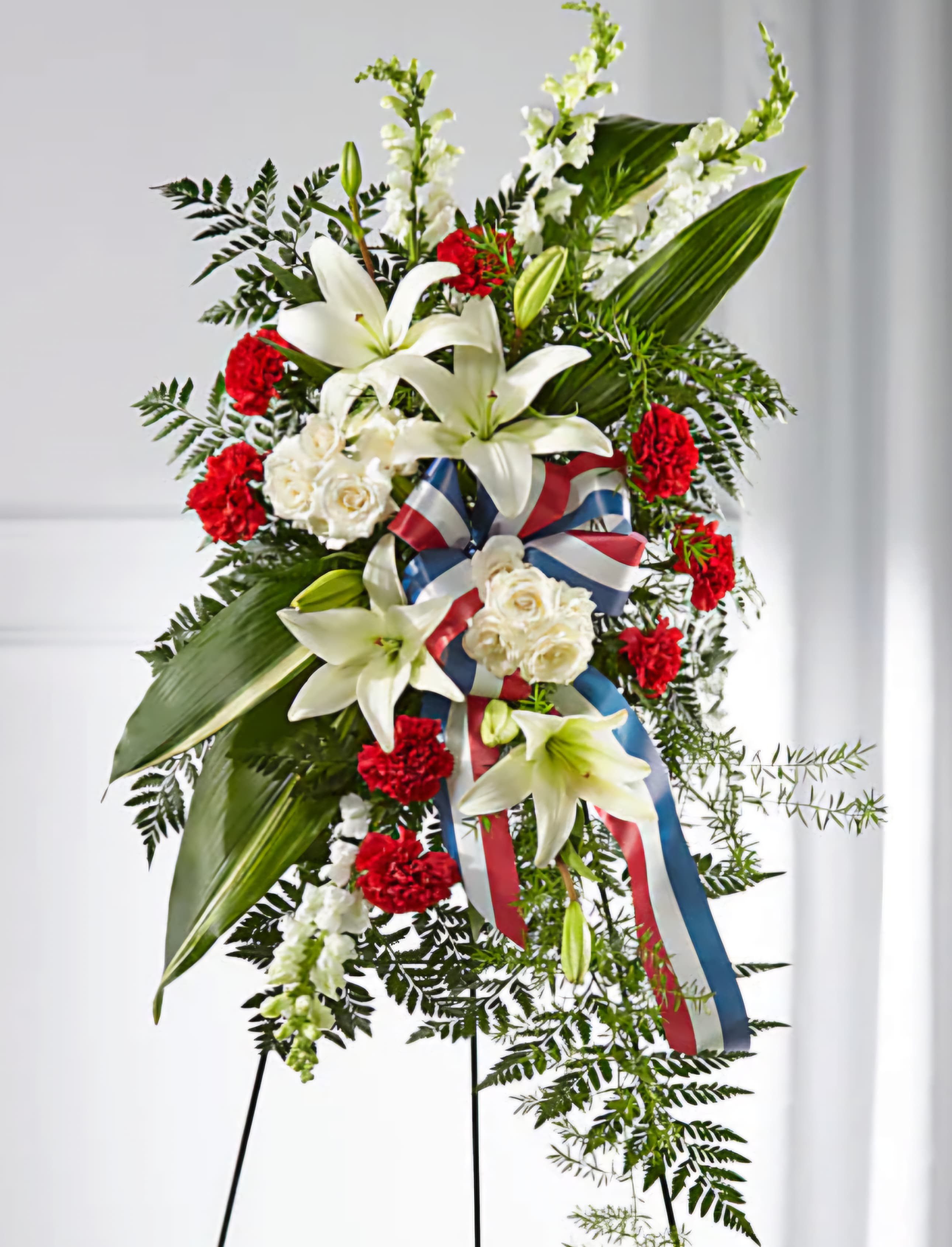 Standing floral spray with white lilies, red carnations, and ribbon on an easel
