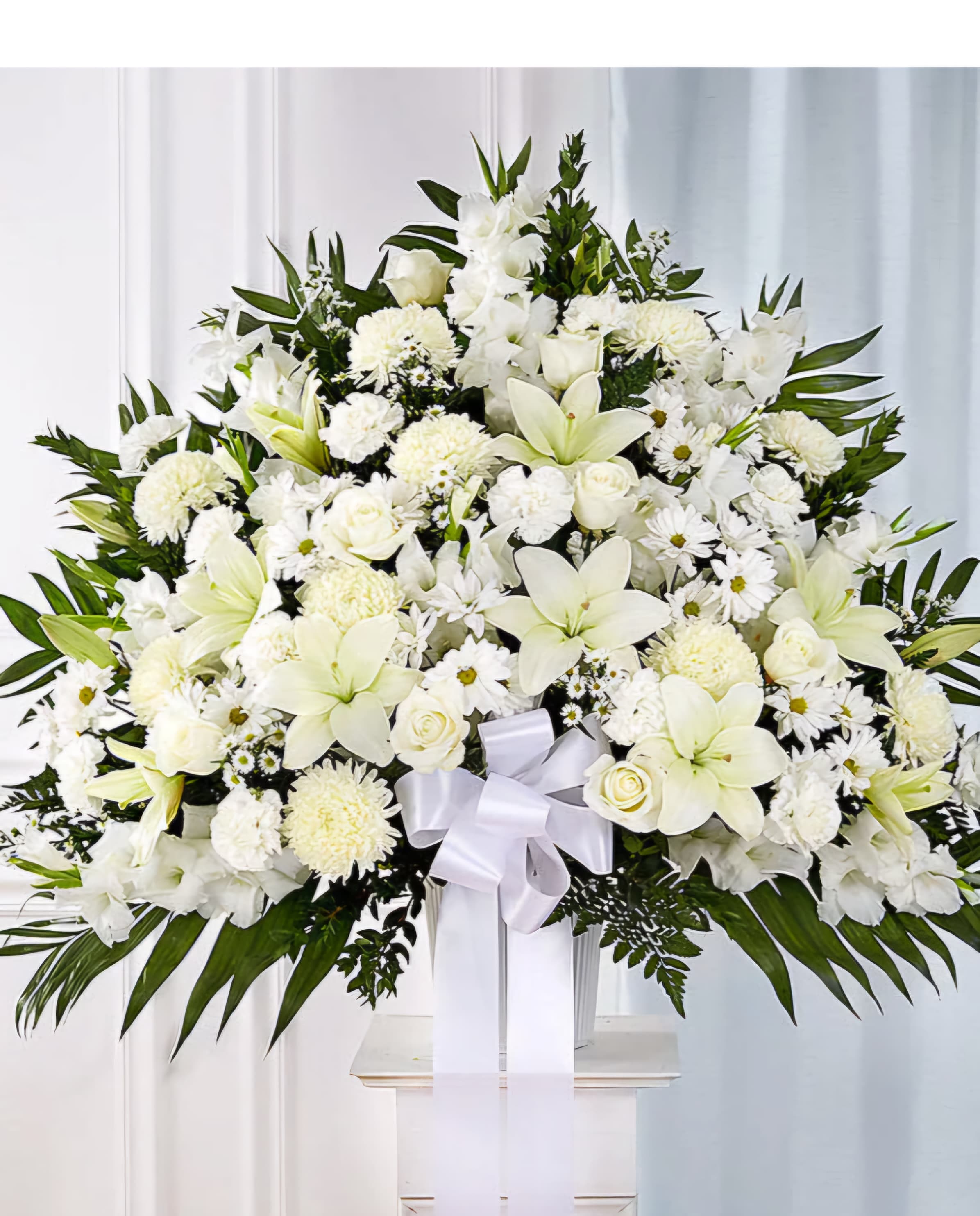 Large white funeral spray with lilies, roses, and daisies on a stand