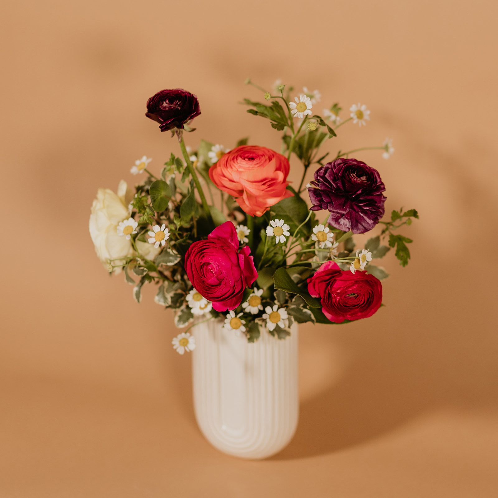 Mixed bouquet of ranunculus and daisies in a white vase