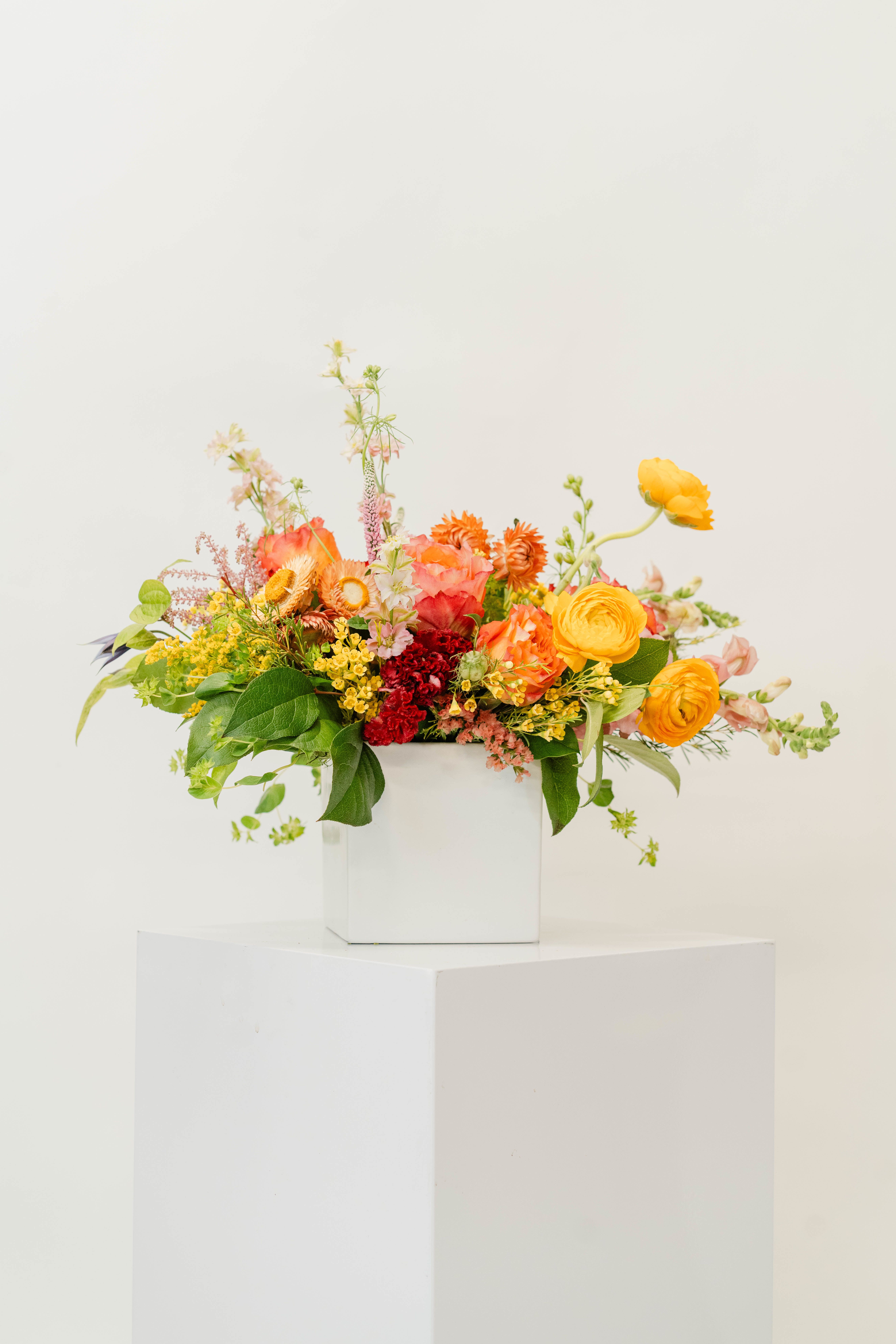 Bright mixed flower arrangement in a white box vase