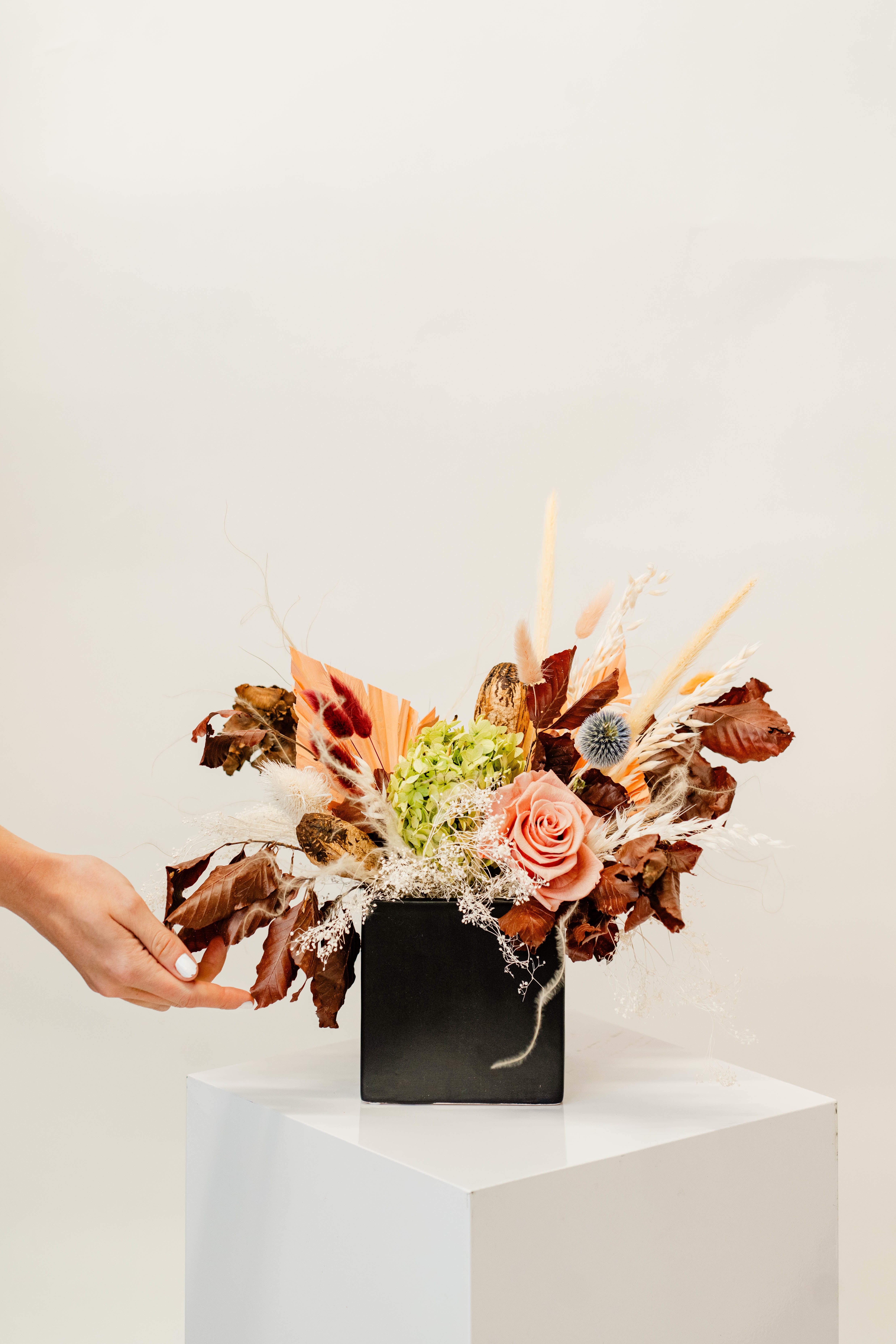 Arrangement of a peach rose and dried flowers in a black vase