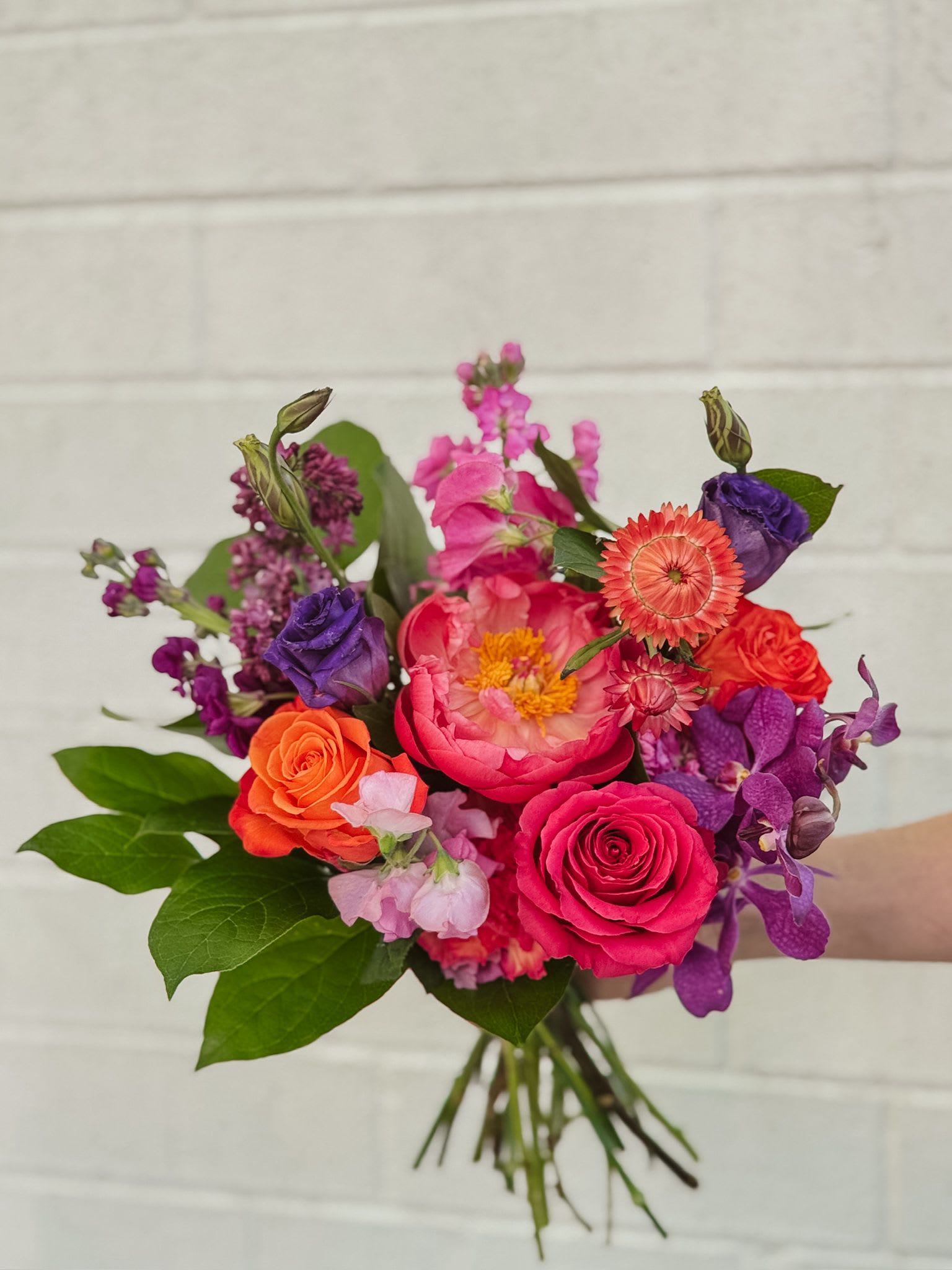Handheld bouquet of pink, orange, and purple flowers