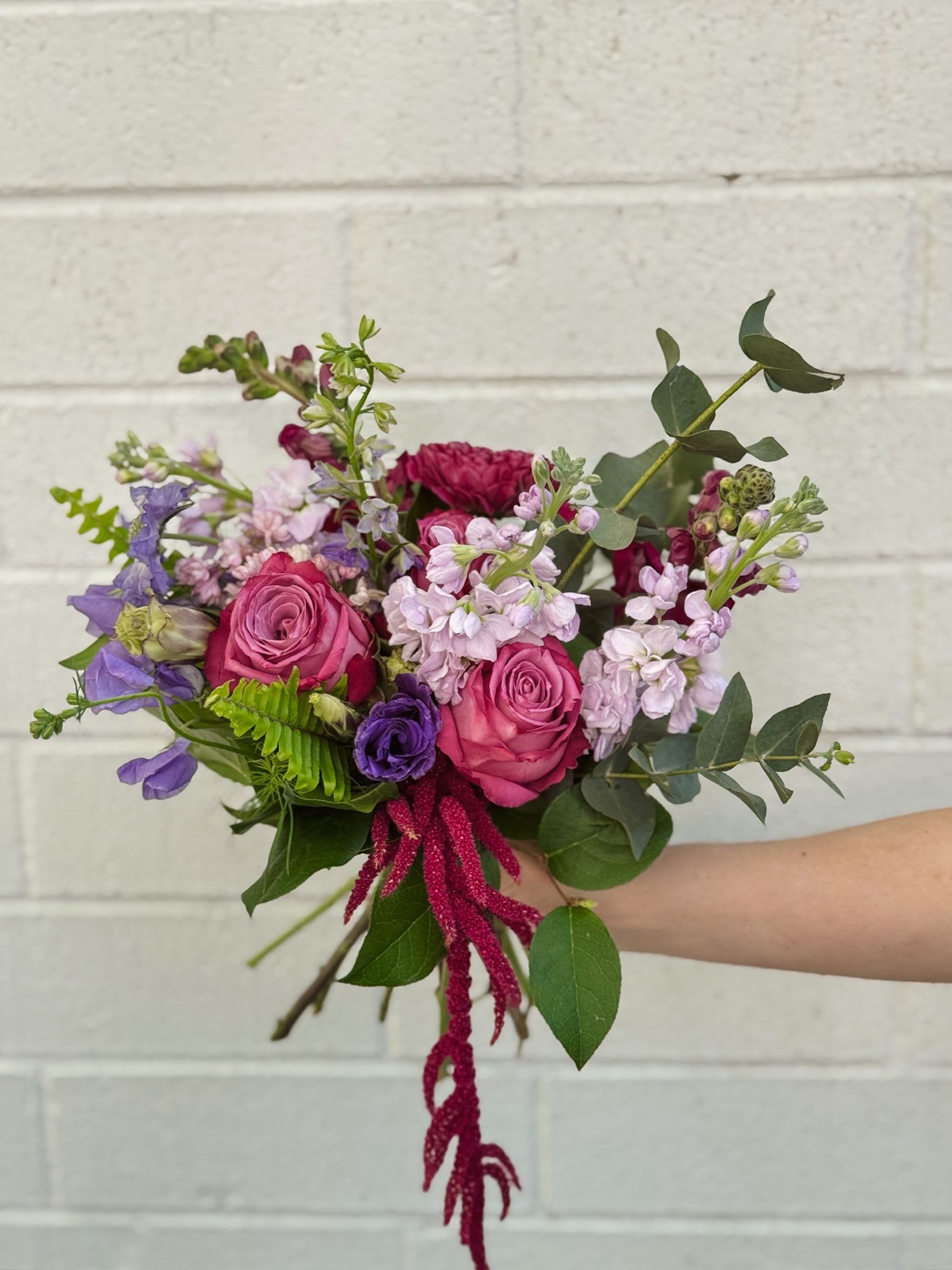 Handheld bouquet of pink and purple flowers with greenery