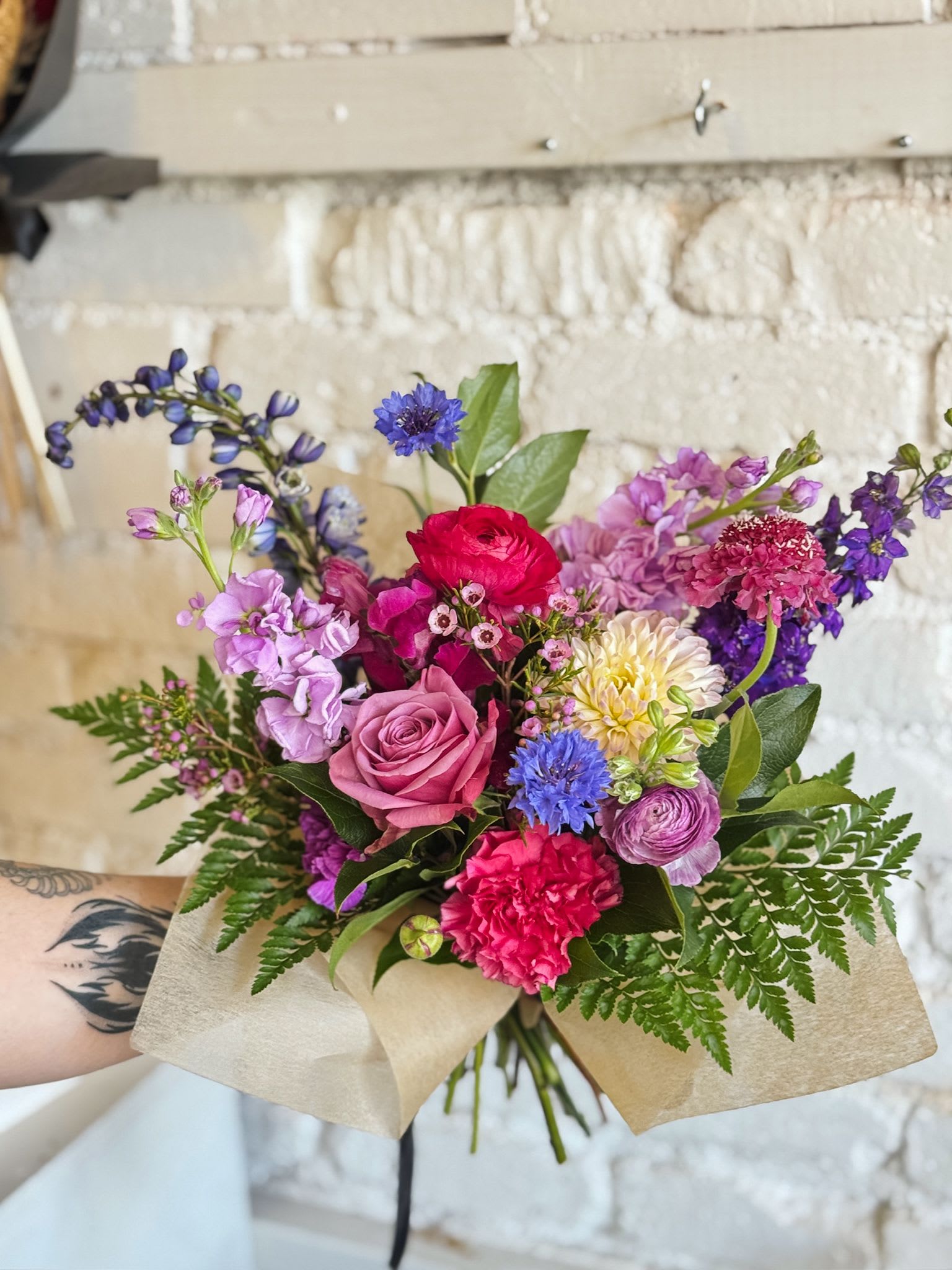 Hand-tied bouquet of pink, purple, and blue flowers wrapped in paper
