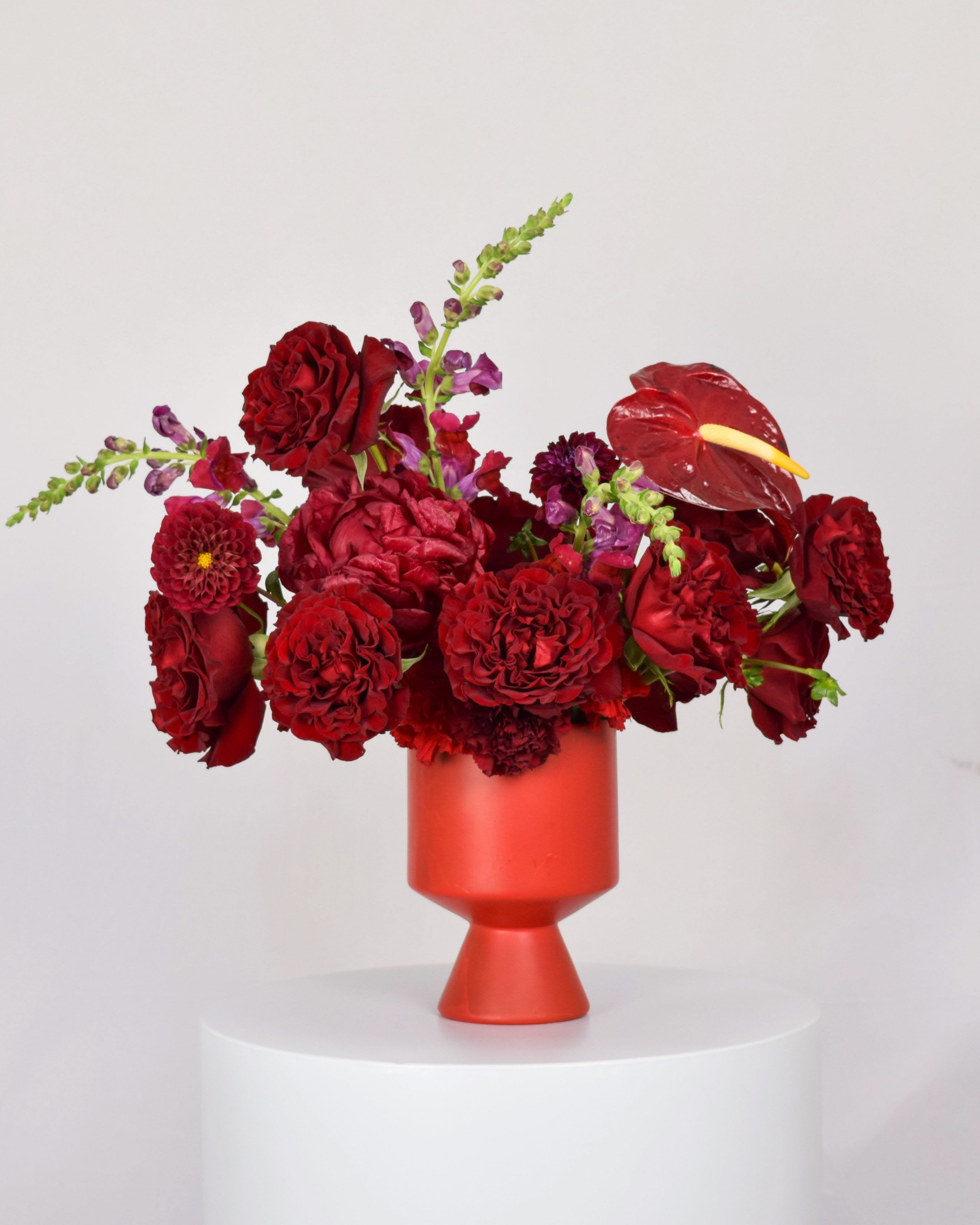 Red floral arrangement in a red vase with anthurium and roses