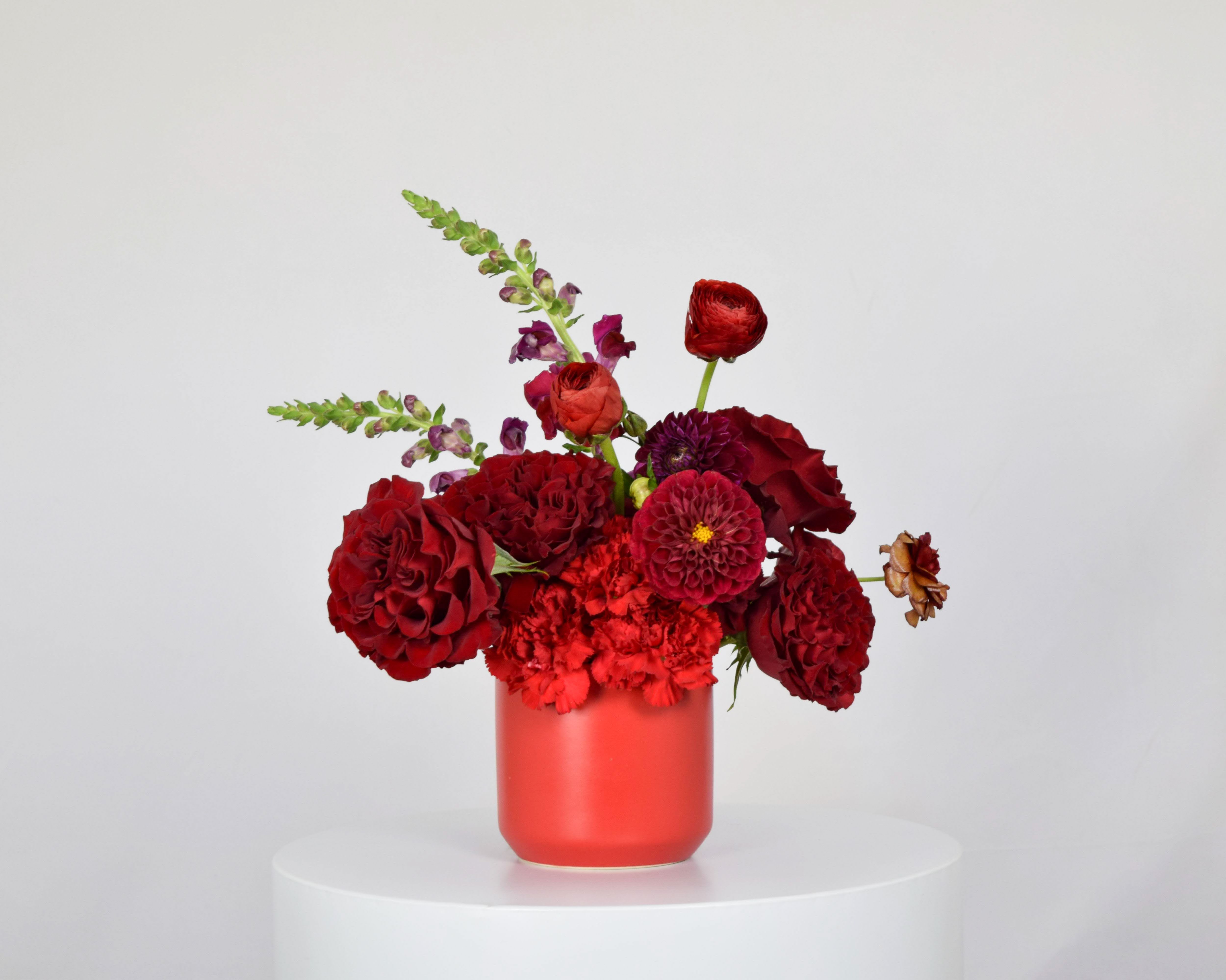 Red floral arrangement in a coral vase with mixed blooms