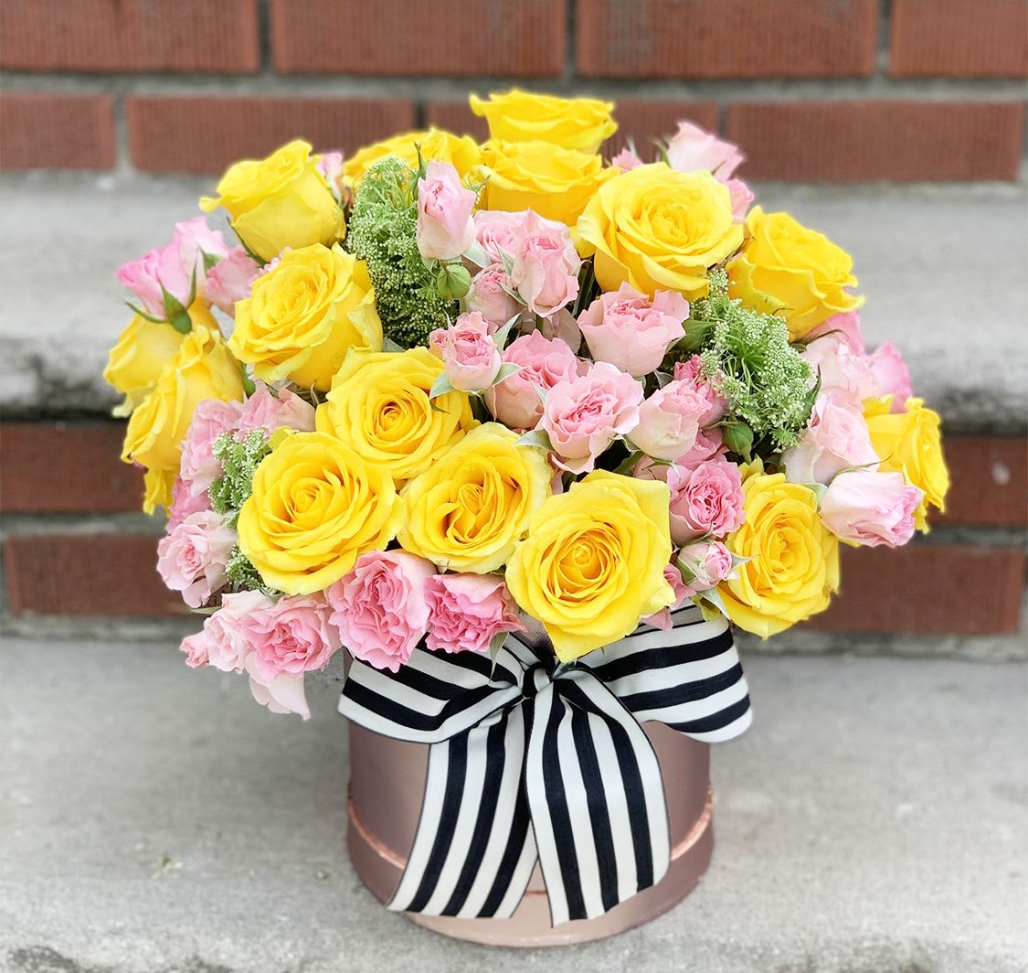Yellow and pink rose bouquet in a round box with a striped ribbon