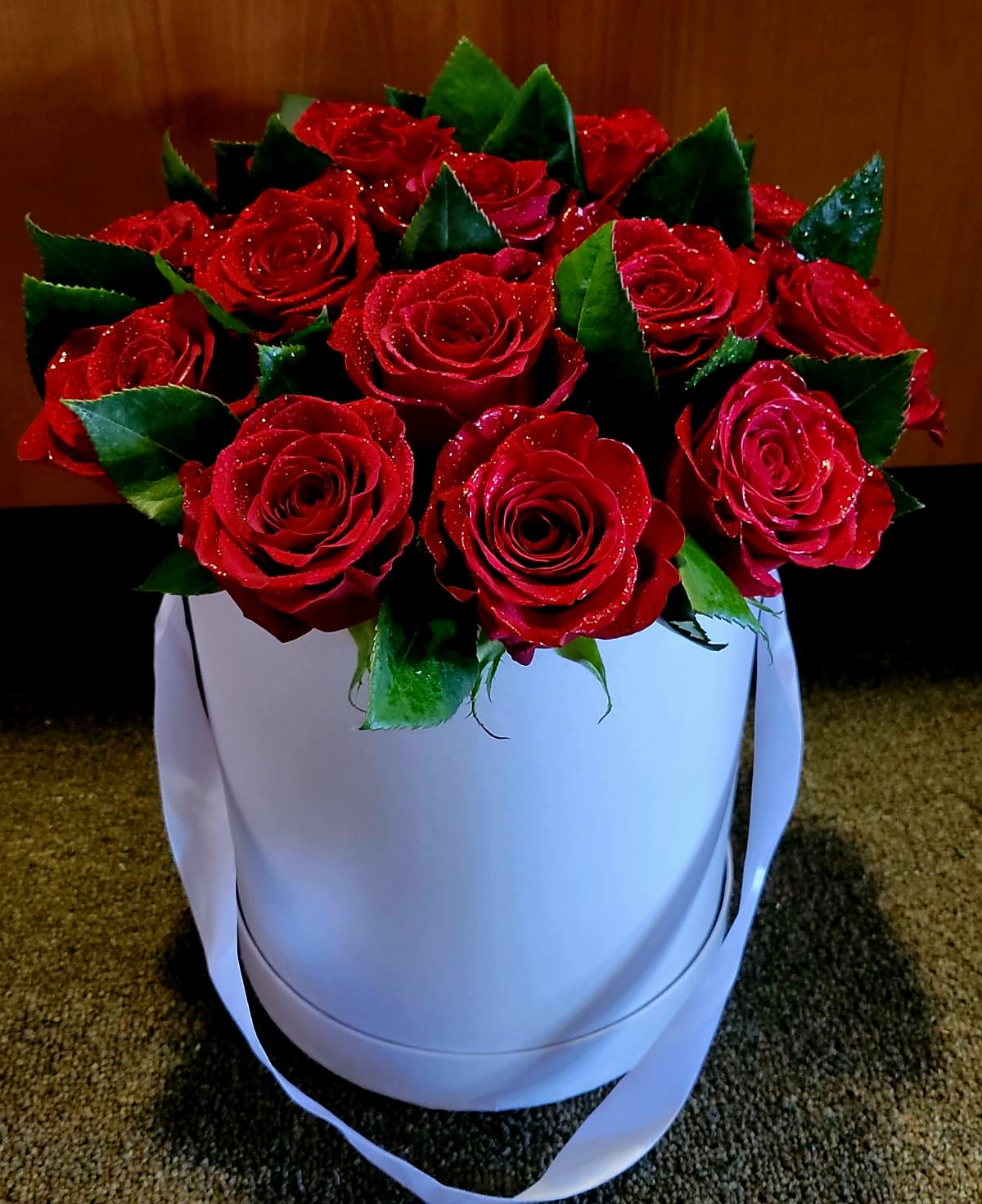 Red roses arranged in a white round box with ribbon handles