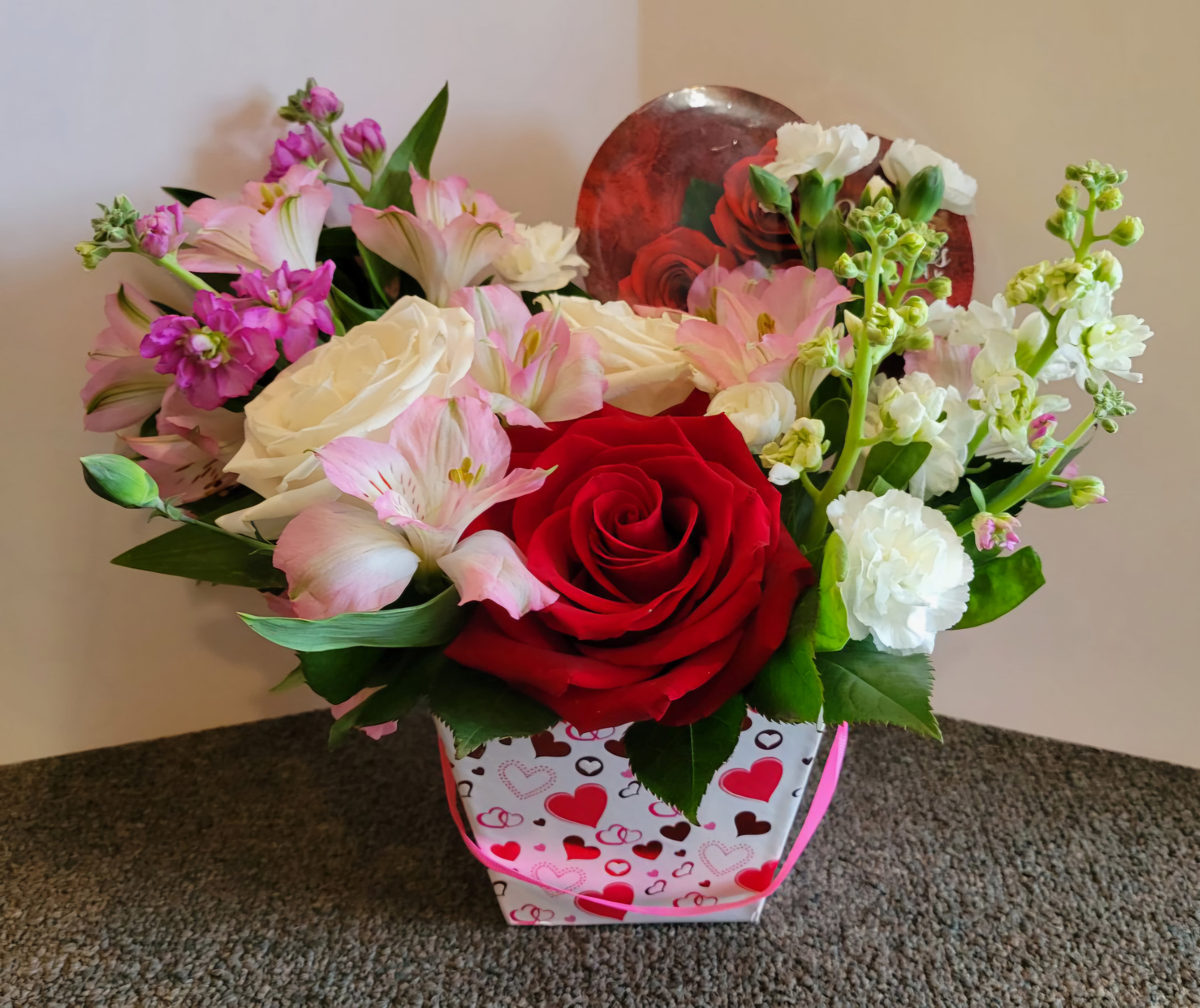 Mixed pink, white, and red flower arrangement in a heart-patterned gift bag