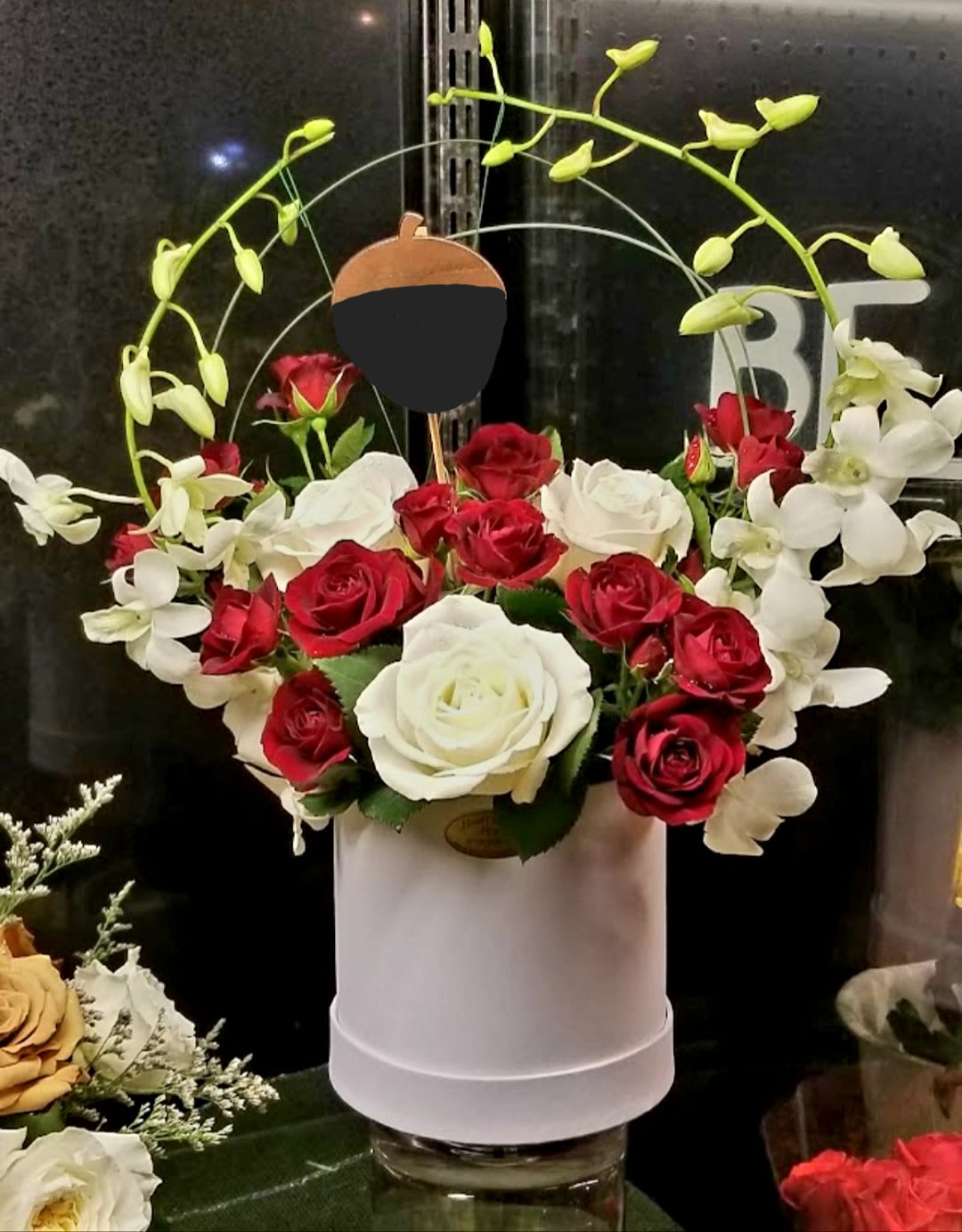 Red and white roses in a white hatbox with arching white orchids
