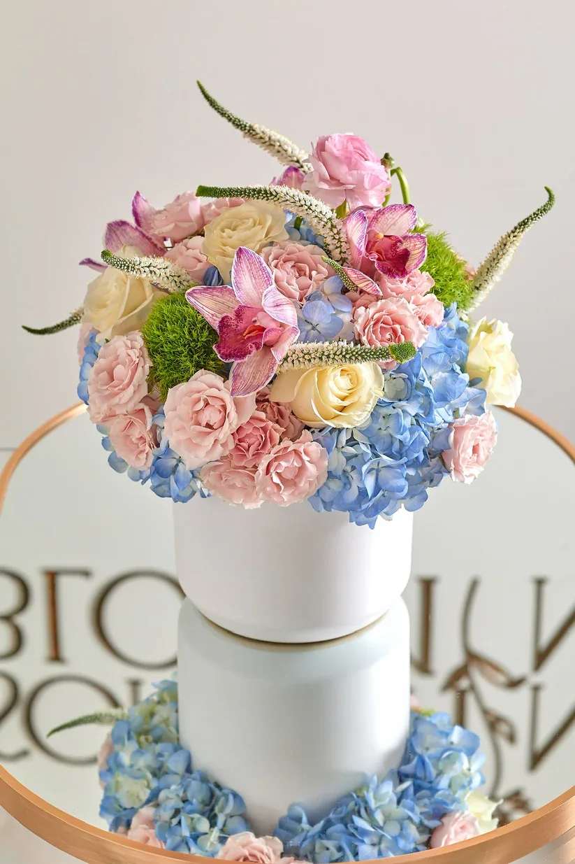 Pastel floral arrangement in a white cylindrical vase with roses and hydrangeas